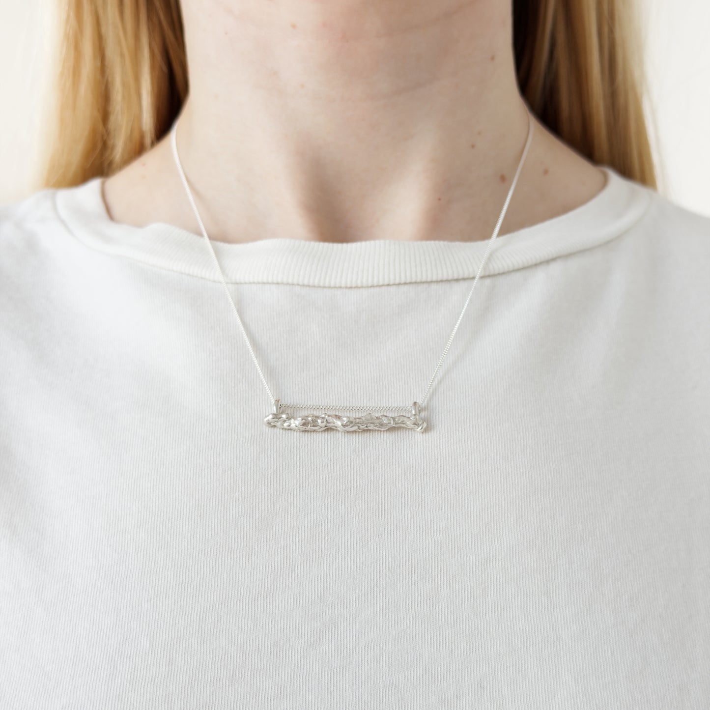 Close up of the Atoll silver necklace, featuring a textured bar pendant. Shown on a person wearing a white top.