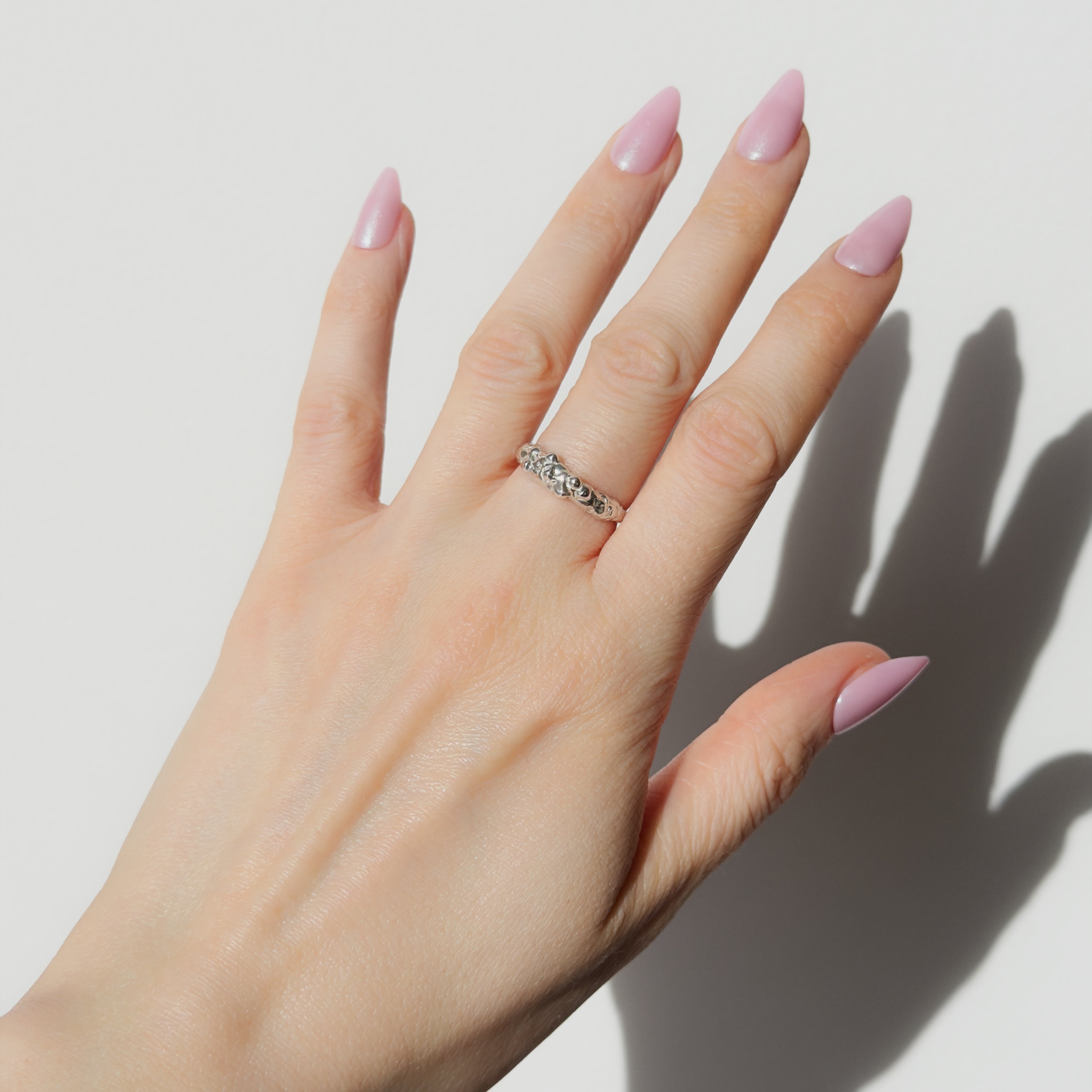 Hand wearing the Atoll textured silver ring on a plain background.