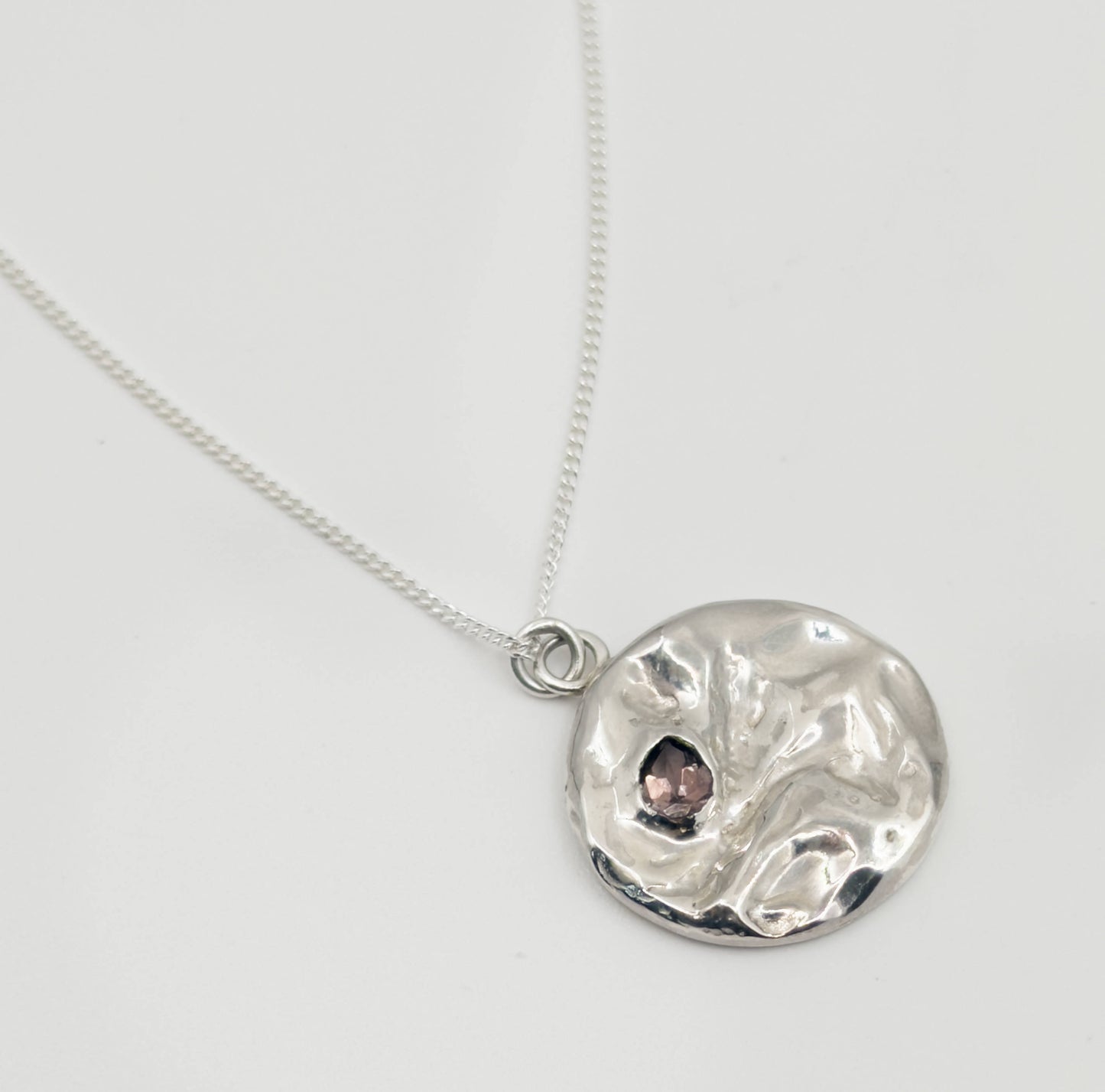 Angled top view of the Devotion silver necklace, featuring a round pendant. Pictured on a light plain background.