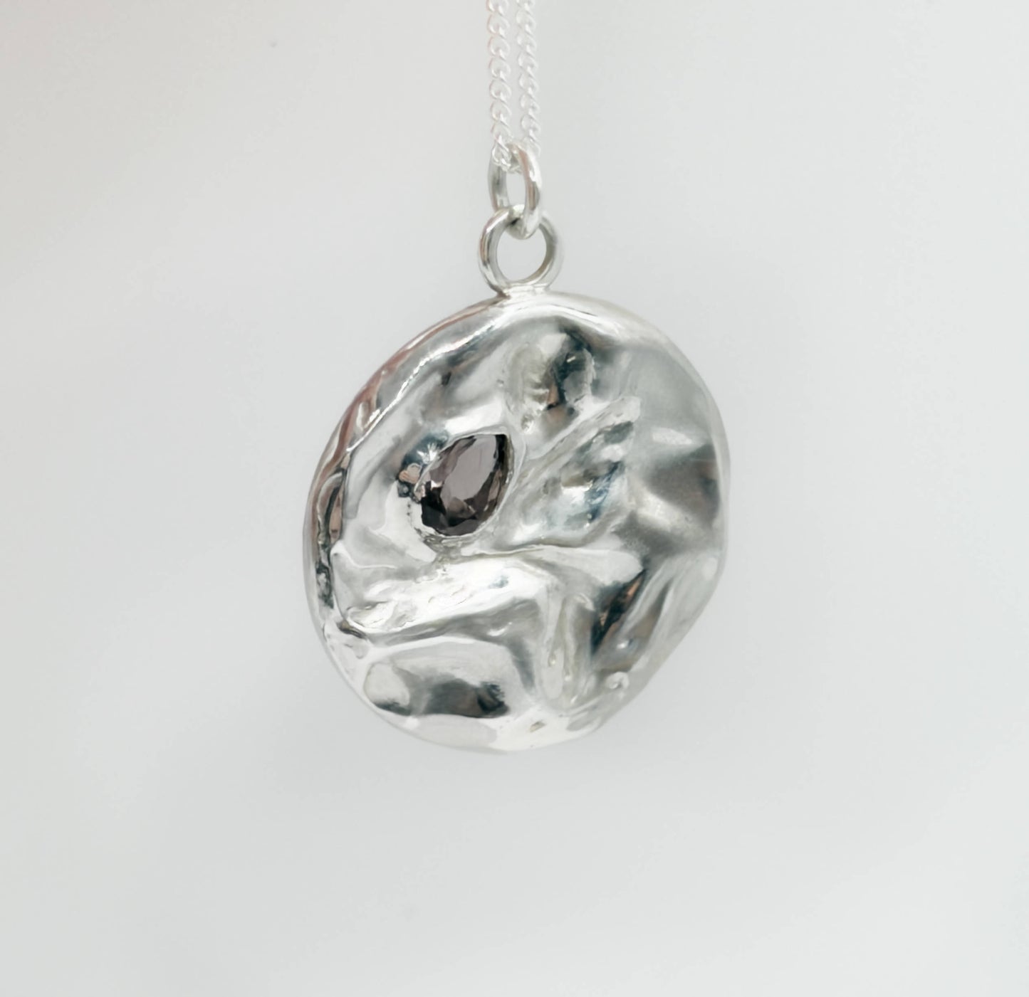 Angled front view of the Devotion silver necklace, featuring a round pendant. Pictured on a light plain background.