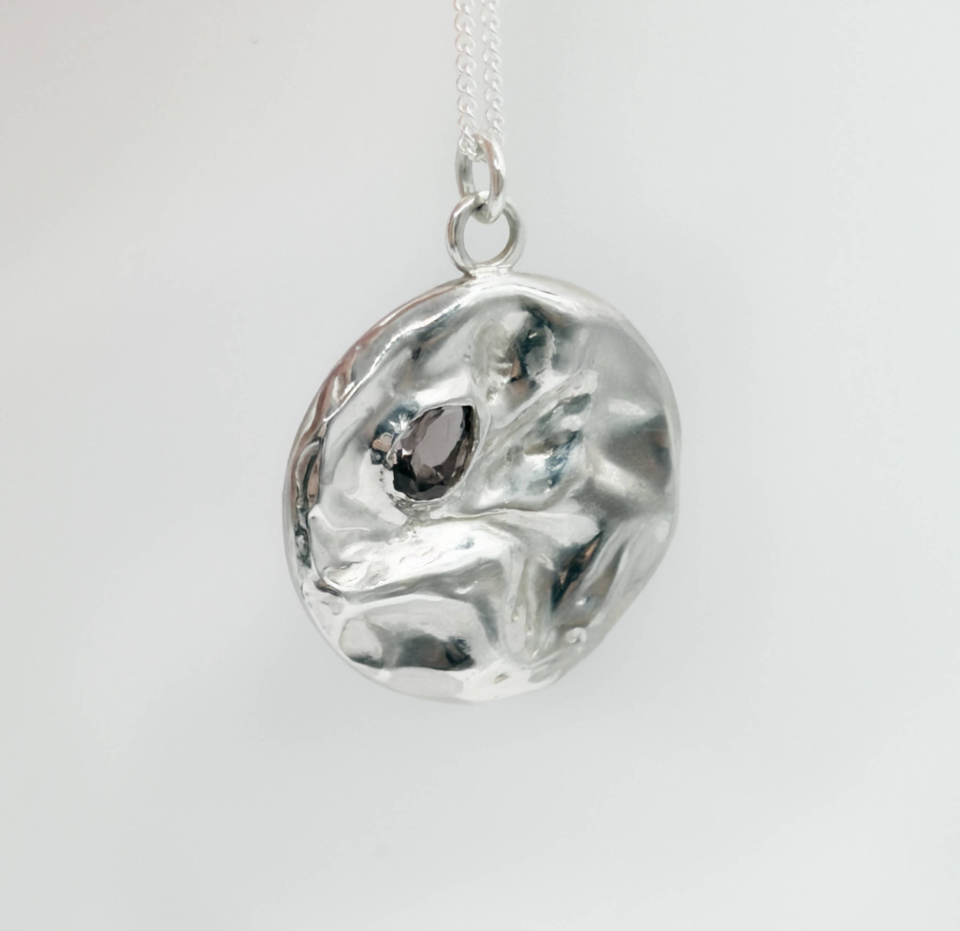 Angled front view of the Devotion silver necklace, featuring a round pendant. Pictured on a light plain background.