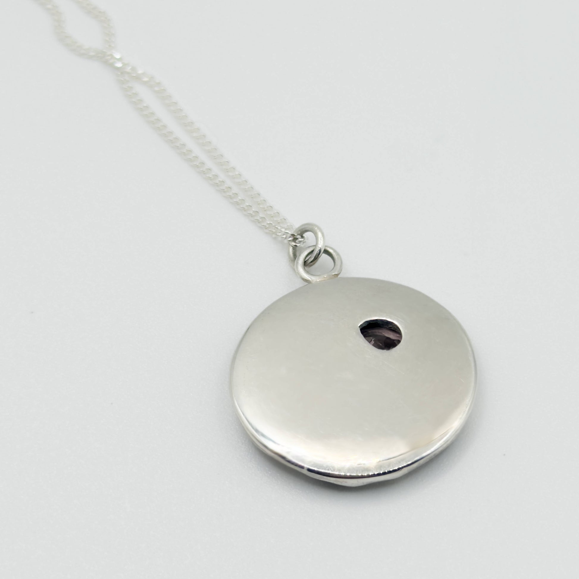 Angled back view of the Devotion silver necklace, featuring a round pendant. Pictured on a light plain background.