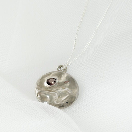 Angled front view of the Devotion silver necklace, featuring a round pendant. Pictured on a light textured background.