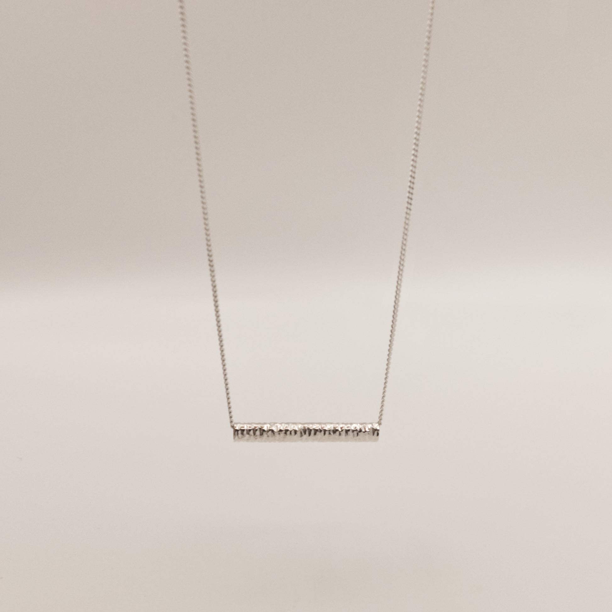 Front view of the Echo textured silver pendant on a curb chain, pictured on a light plain background.