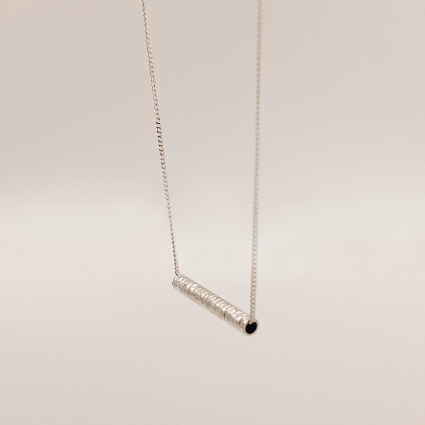 Angled front view of the Echo textured silver pendant on a curb chain, pictured on a light plain background.