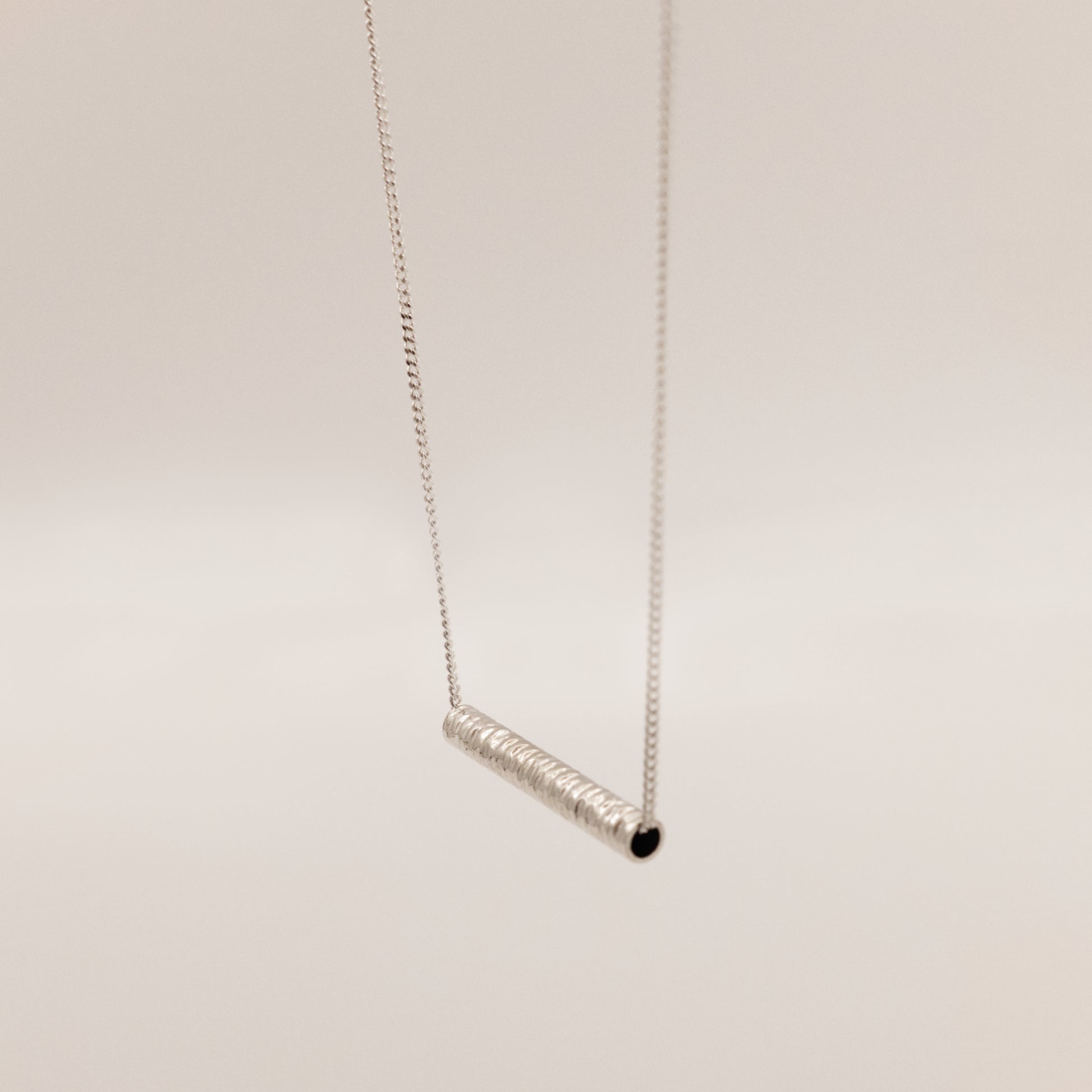 Angled front view of the Echo textured silver pendant on a curb chain, pictured on a light plain background.