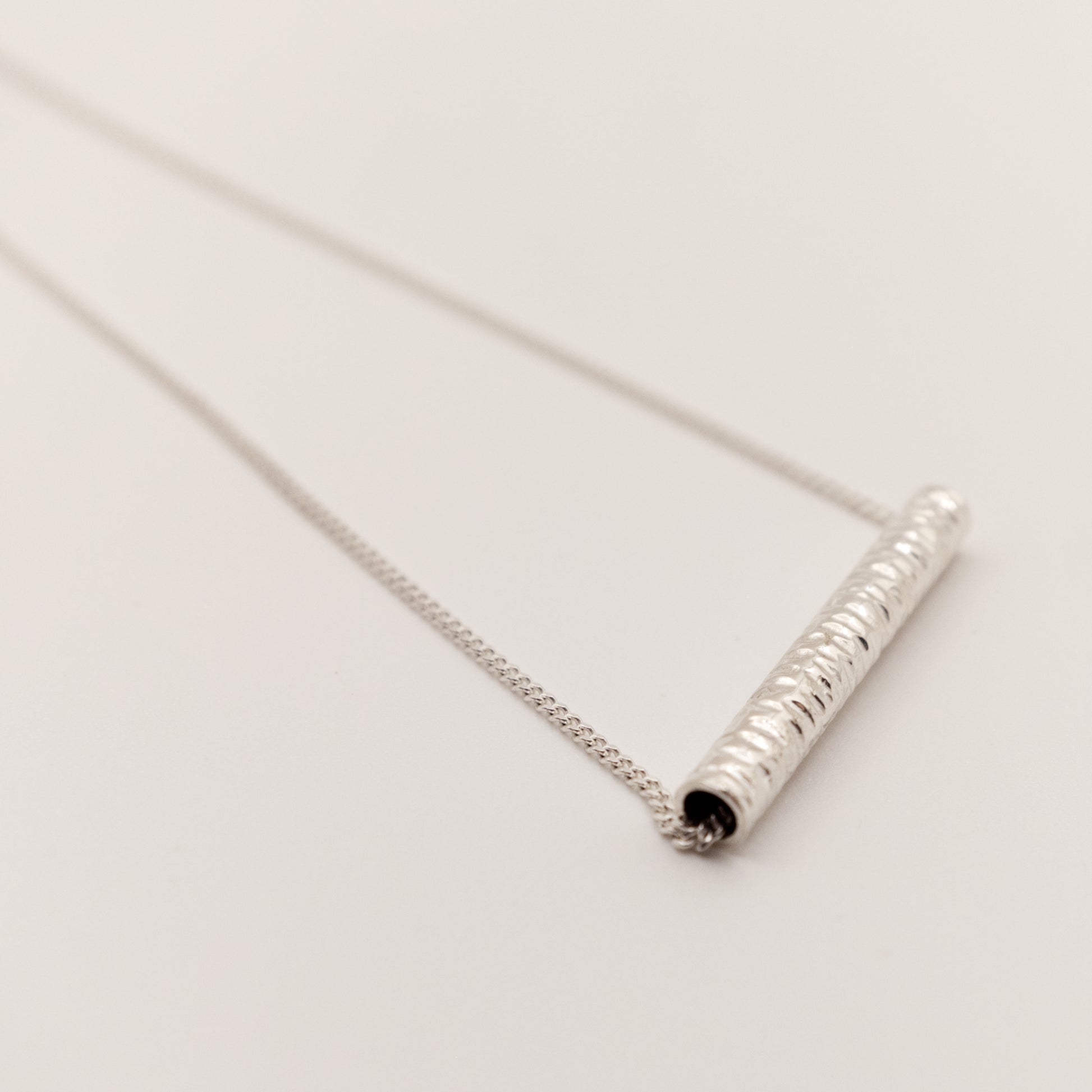 Close-up of the Echo textured silver pendant on a curb chain, pictured on a light plain background.