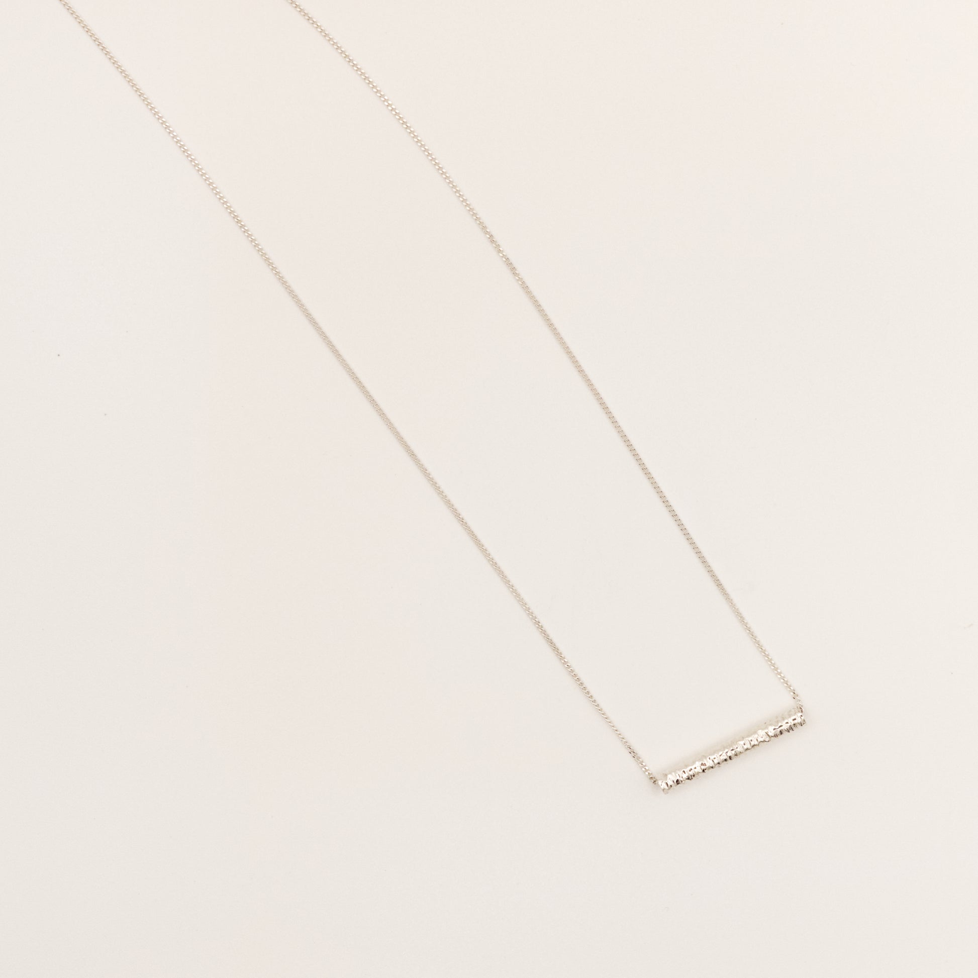 Top view of the Echo textured silver pendant on a curb chain, pictured on a light plain background.