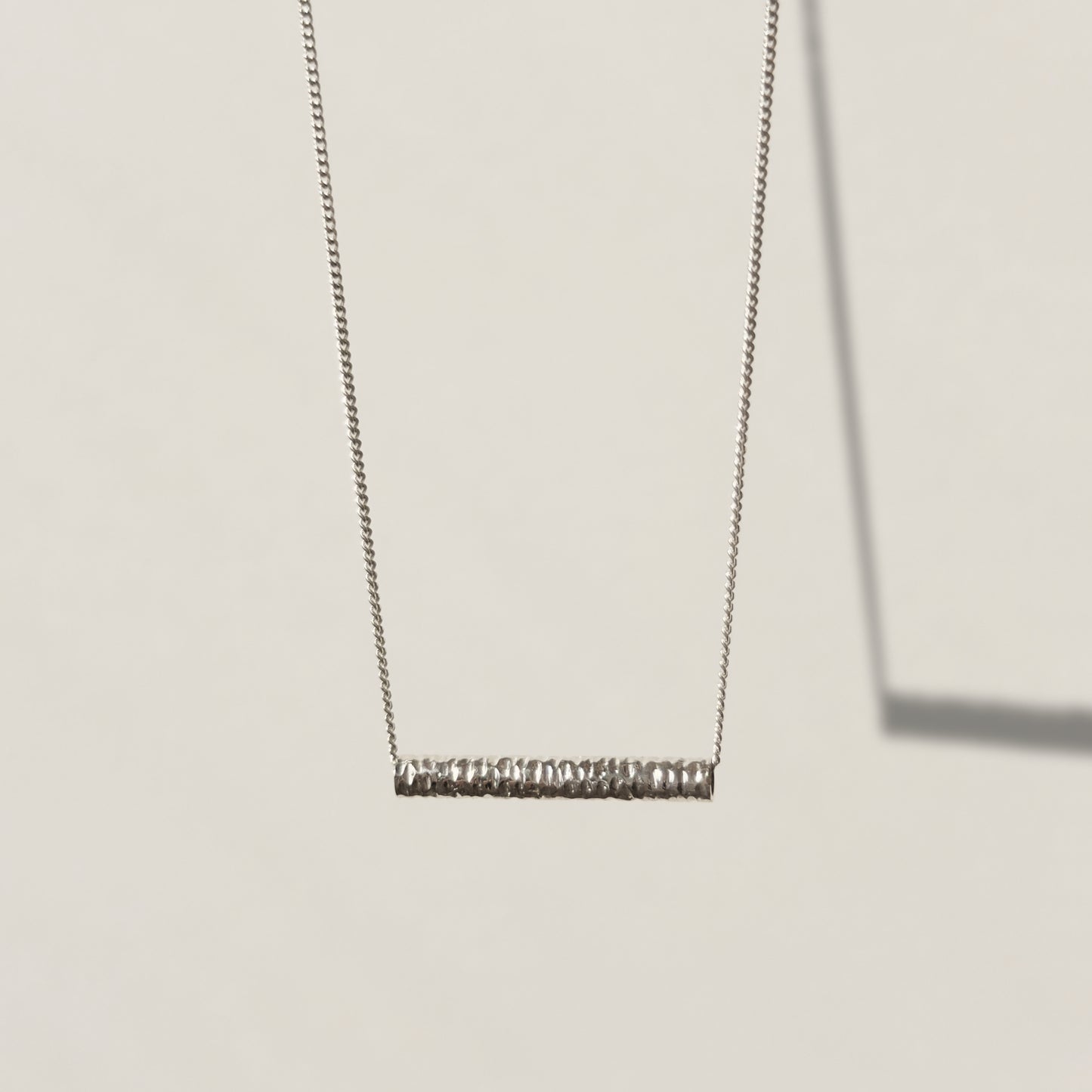 Front view of the Echo textured silver pendant on a curb chain, pictured on a light plain background.