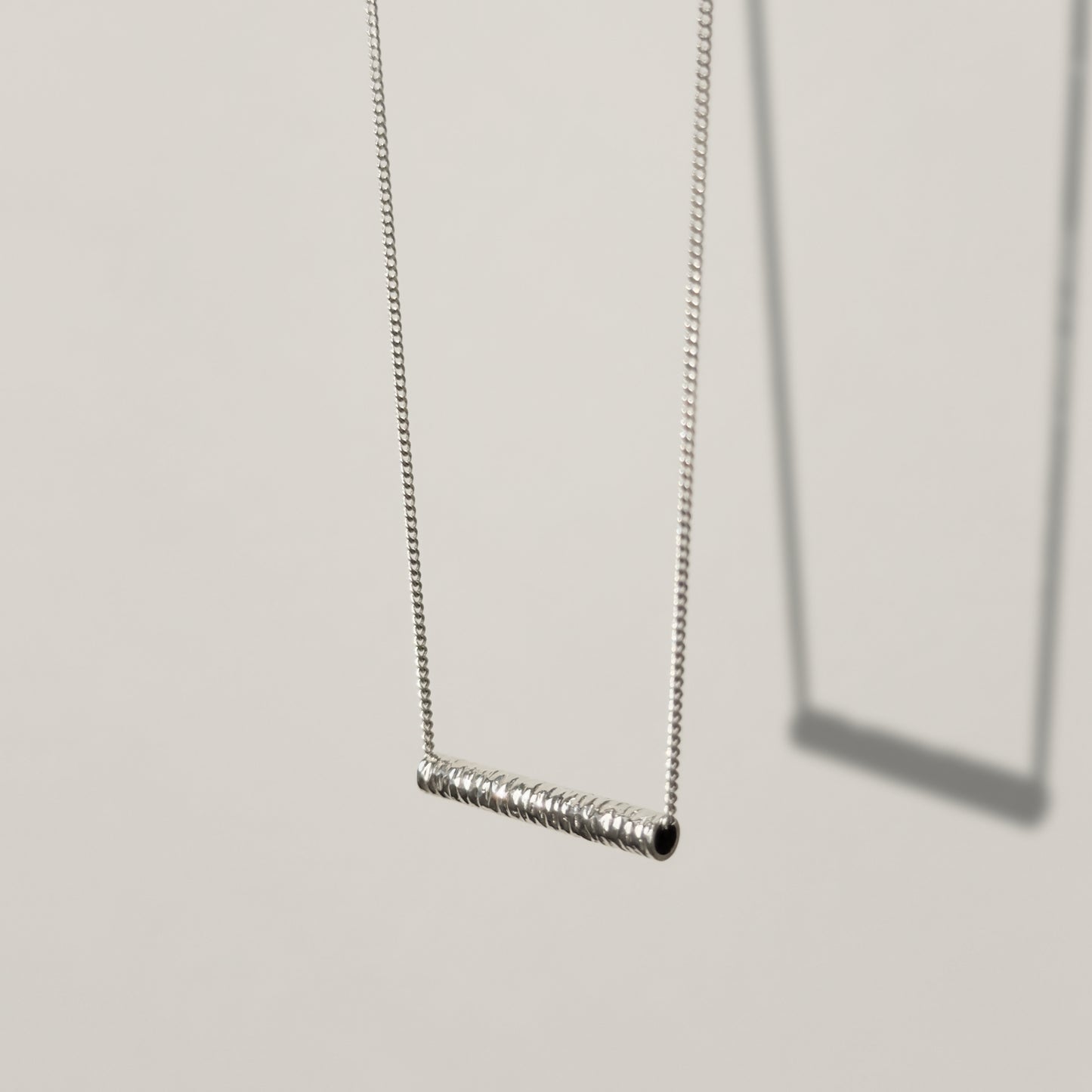 Angled front view of the Echo textured silver pendant on a curb chain, pictured on a light plain background.