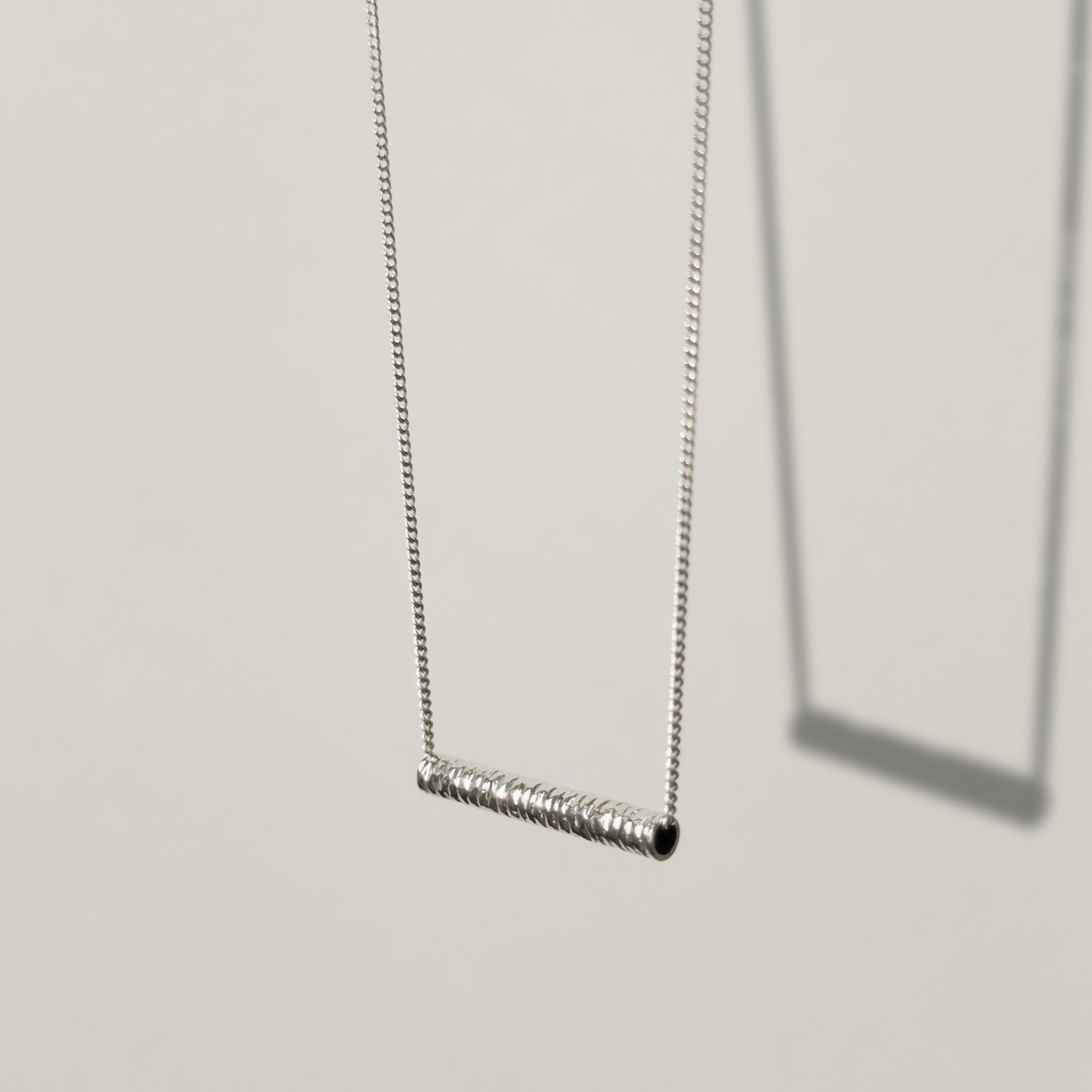 Angled front view of the Echo textured silver pendant on a curb chain, pictured on a light plain background.