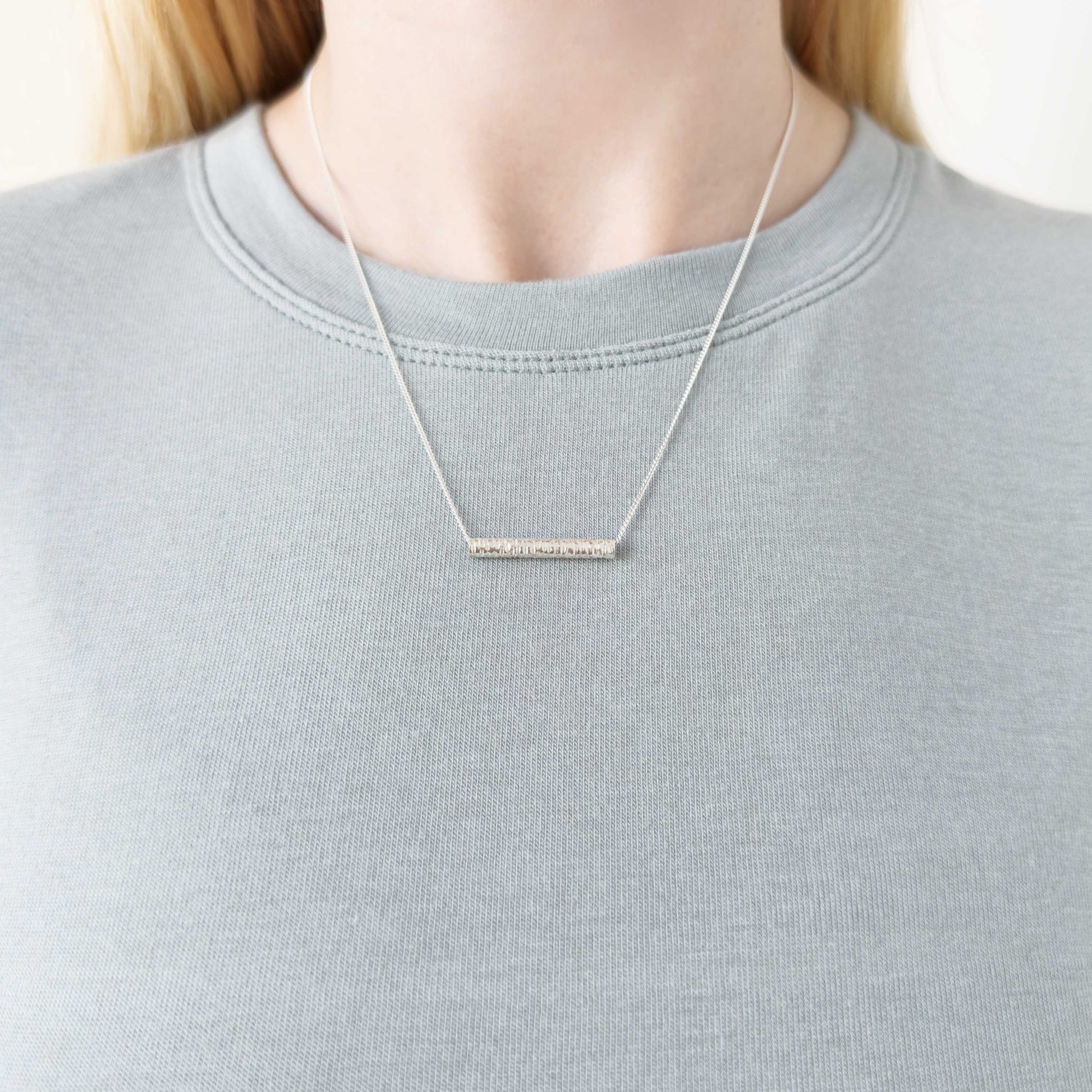 Echo textured silver pendant on a curb chain. Pictured on a person wearing a light blue-gray top.