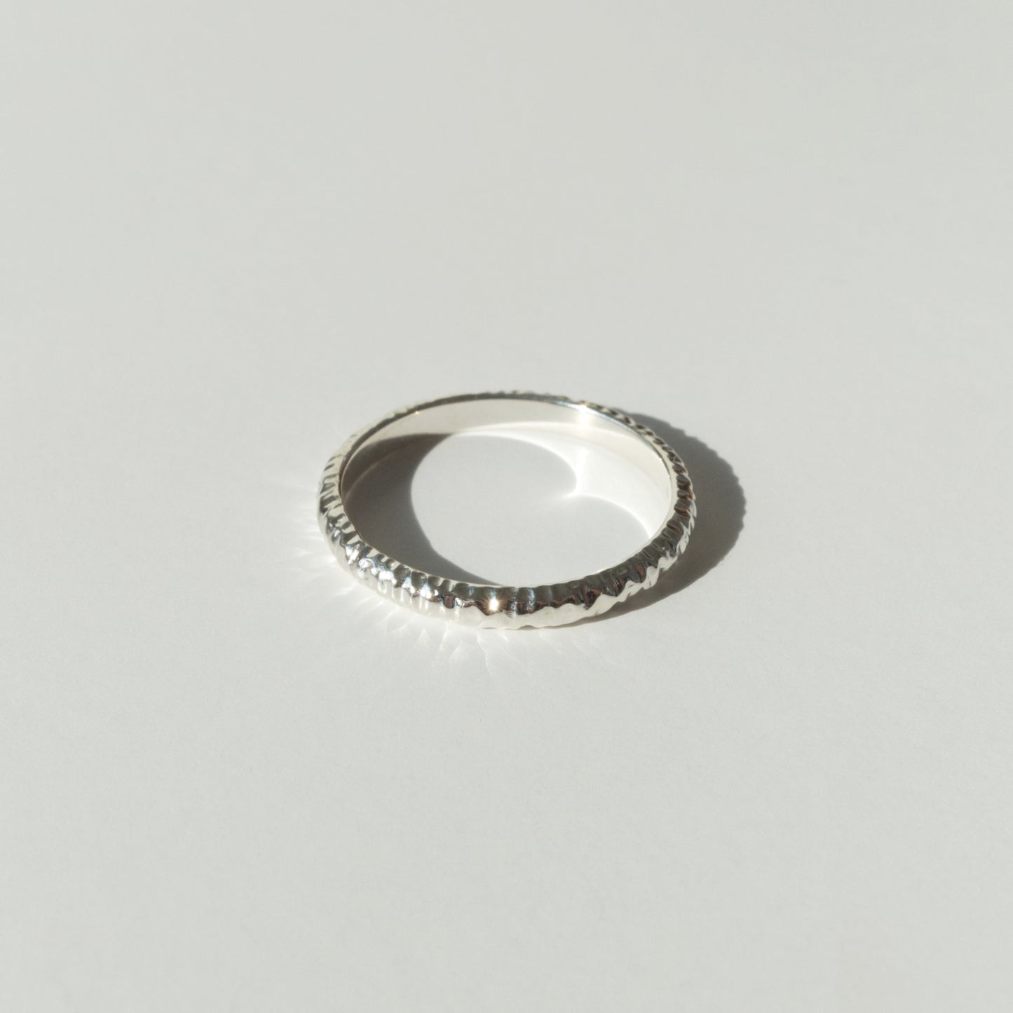 Front view of the Echo ring - a thin silver band ring with a textured surface, photographed on a plain light gray background.
