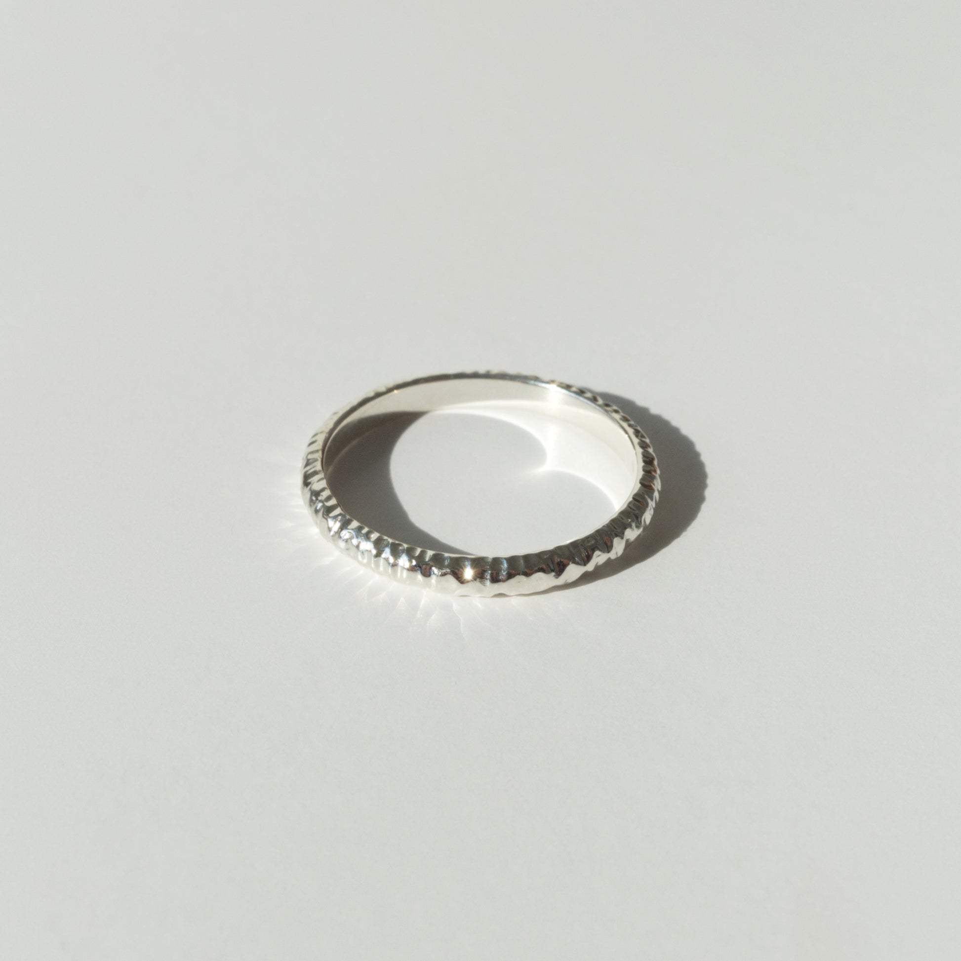 Front view of the Echo ring - a thin silver band ring with a textured surface, photographed on a plain light gray background.