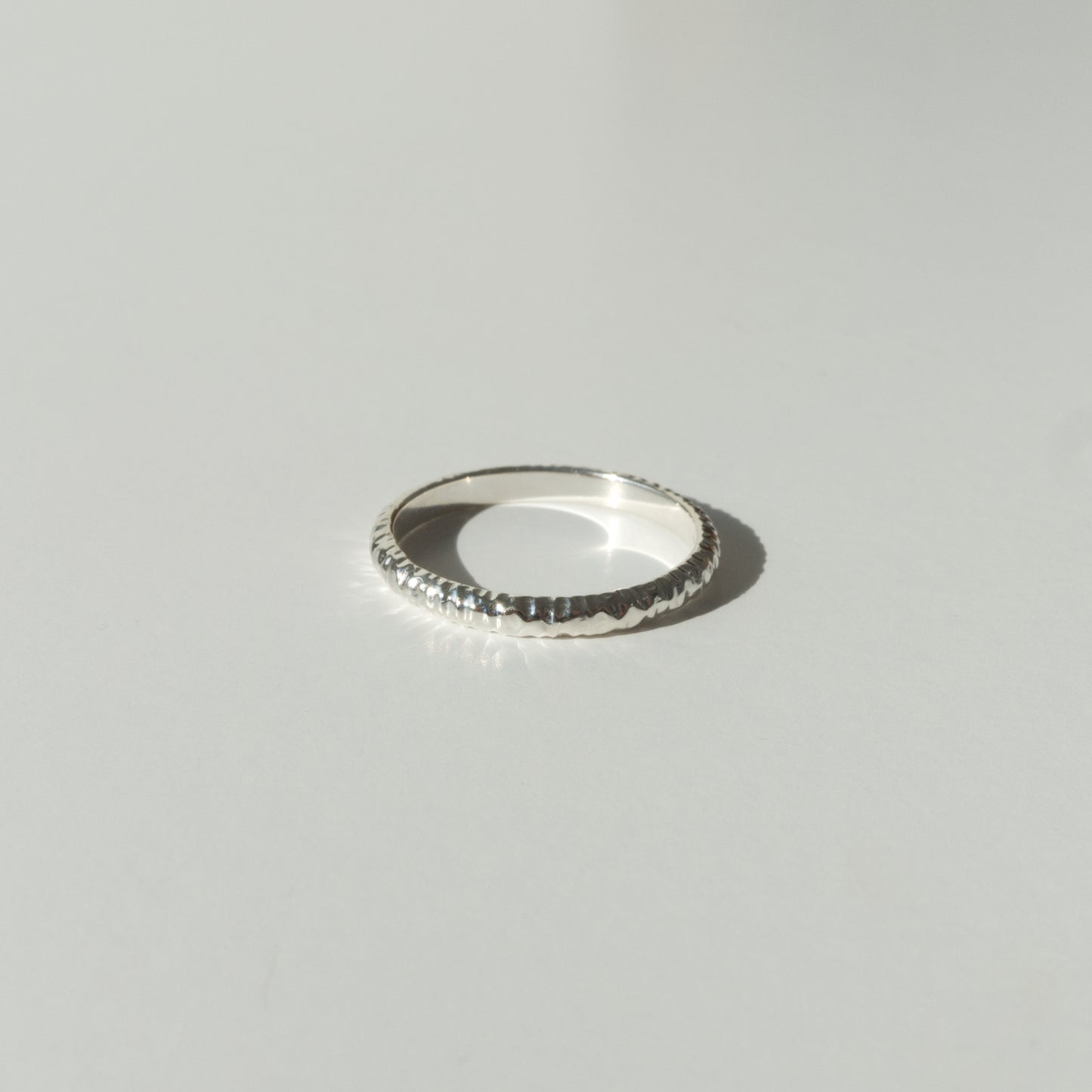 Front view of the Echo ring - a thin silver band ring with a textured surface, photographed on a plain light gray background.