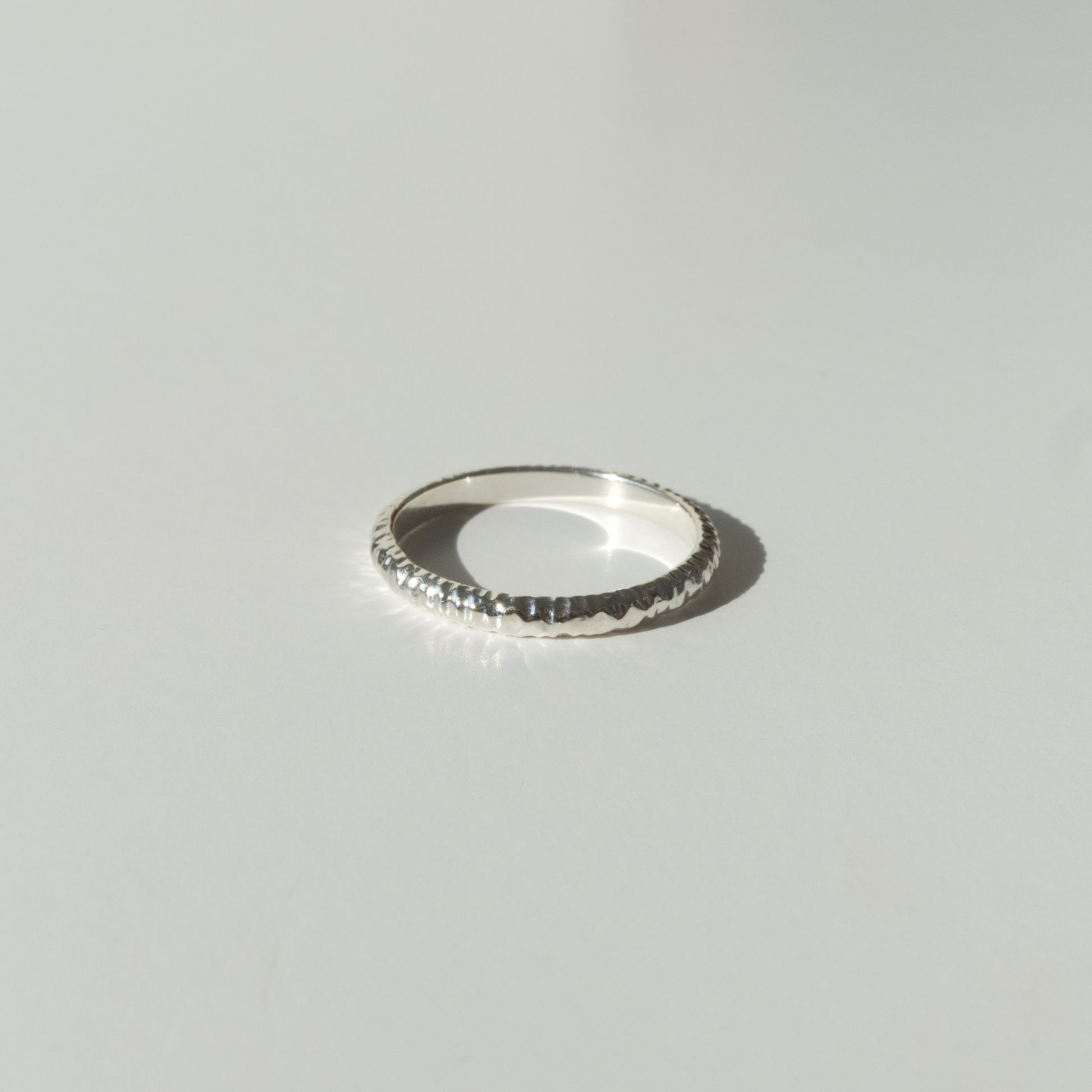 Front view of the Echo ring - a thin silver band ring with a textured surface, photographed on a plain light gray background.