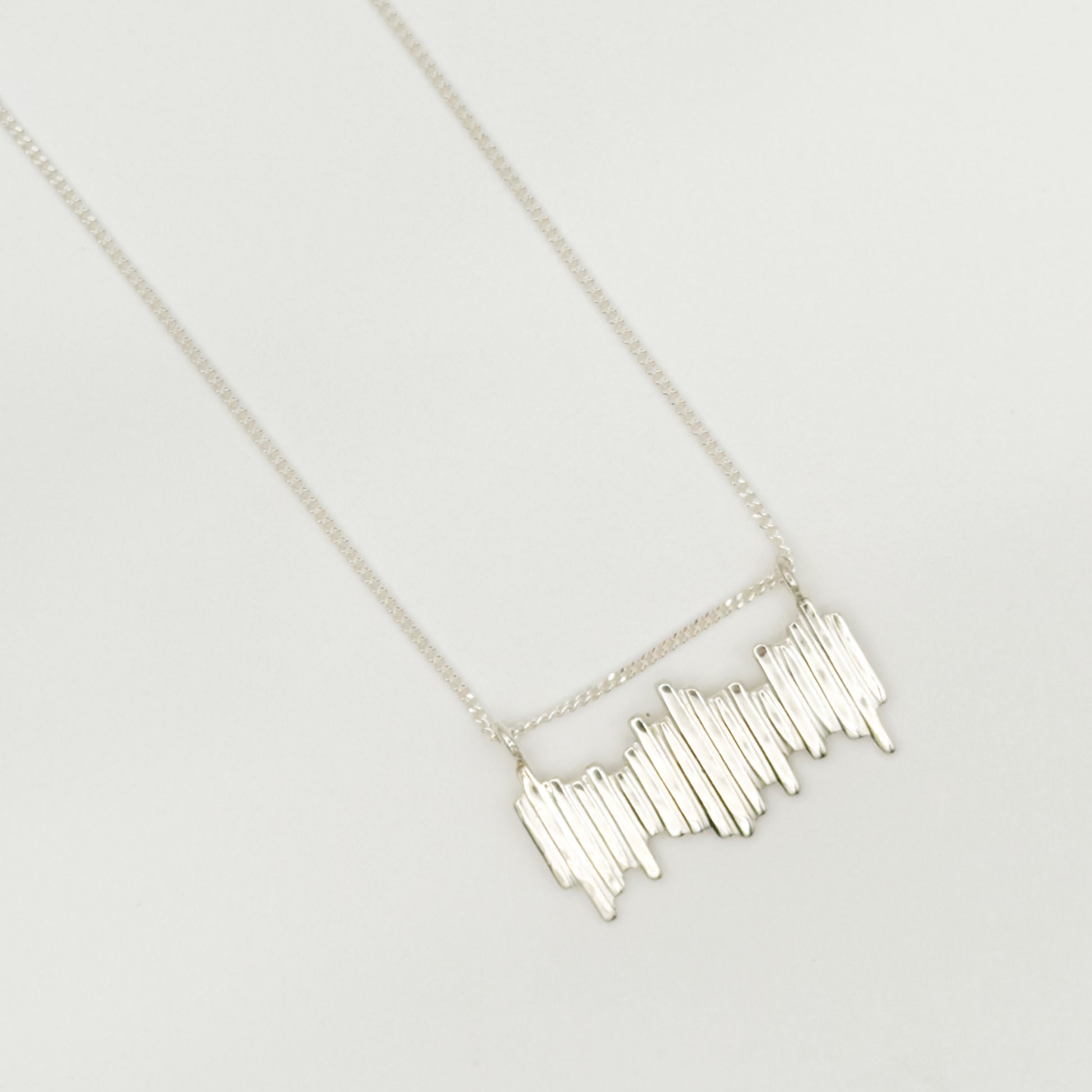 Close up top view of the Guidance textured silver necklace, pictured on a light plain background.