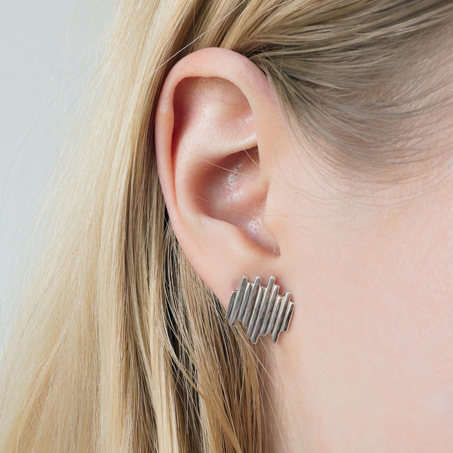 Close-up of an ear wearing the Guidance silver stud earring with blonde hair.
