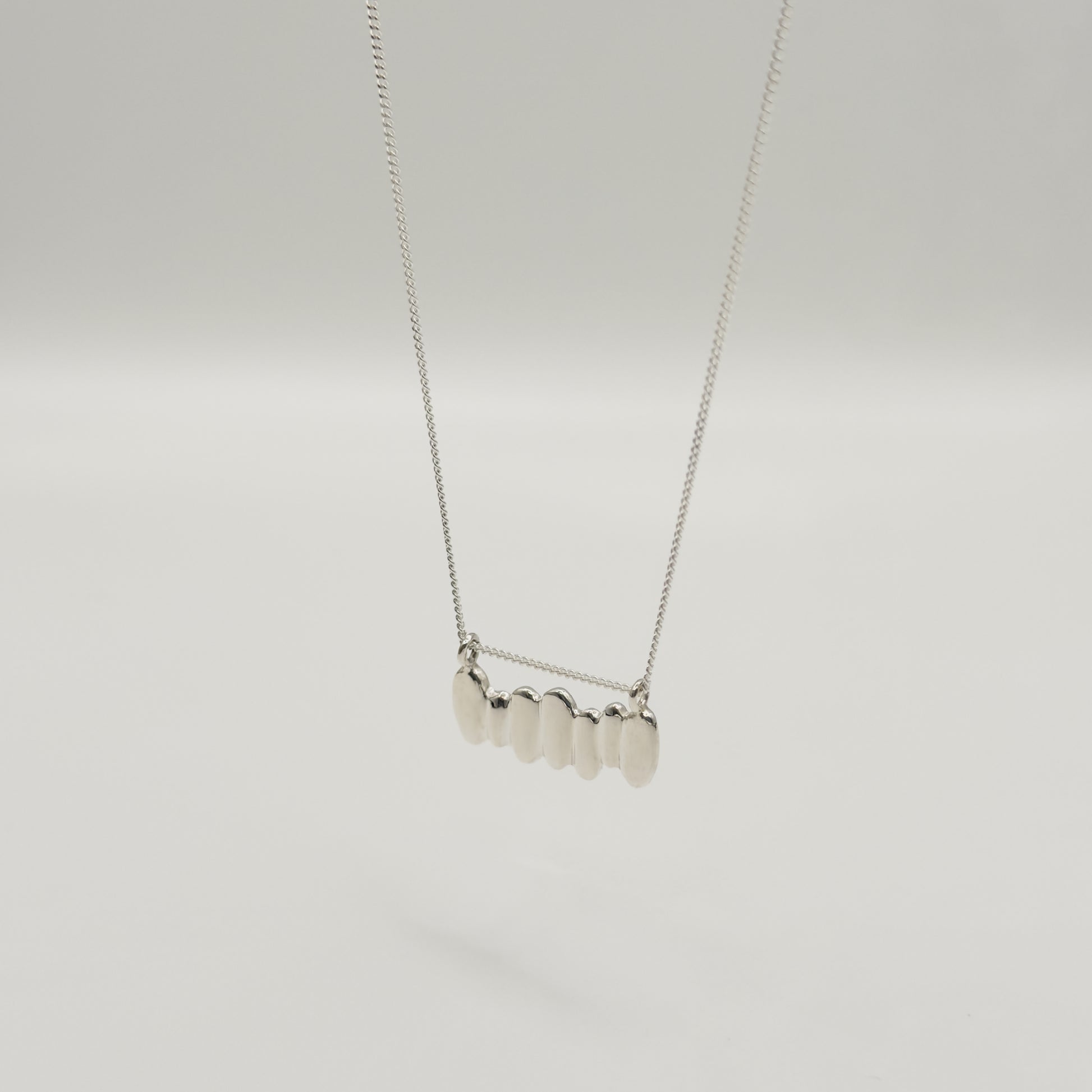 Angled front view of the Meridian textured silver necklace, pictured on a light plain background.