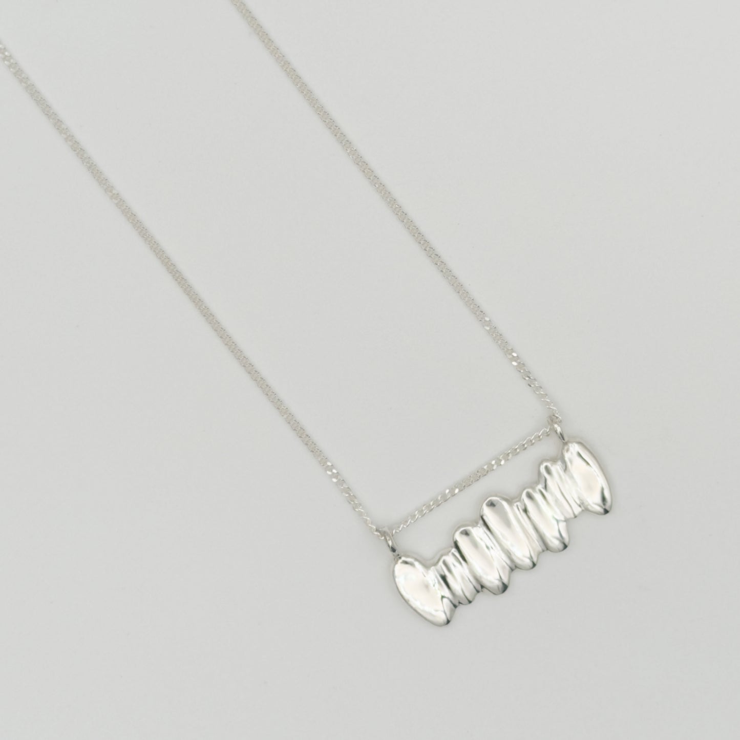 Top view close-up of the Meridian textured silver necklace, pictured on a light plain background.