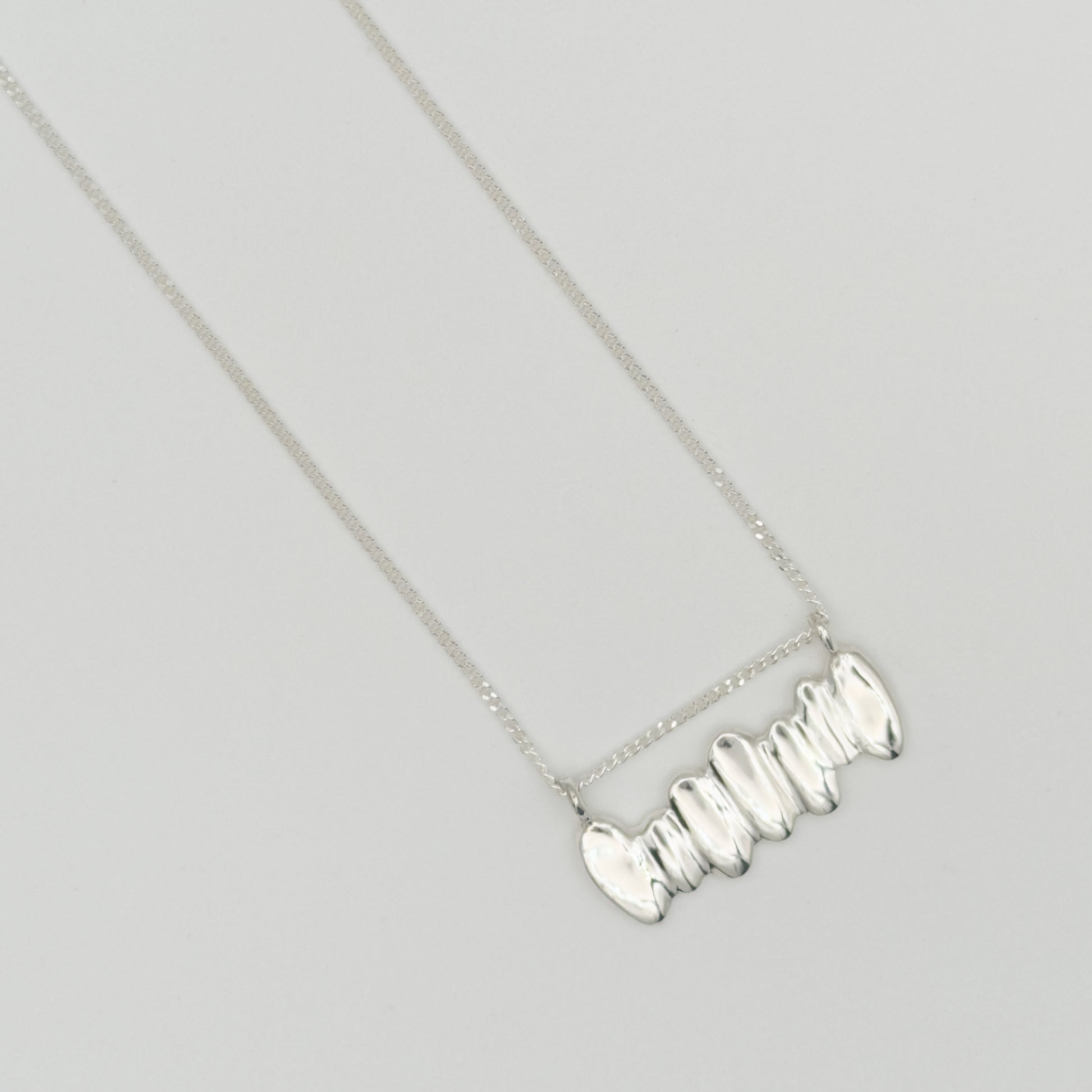 Top view close-up of the Meridian textured silver necklace, pictured on a light plain background.