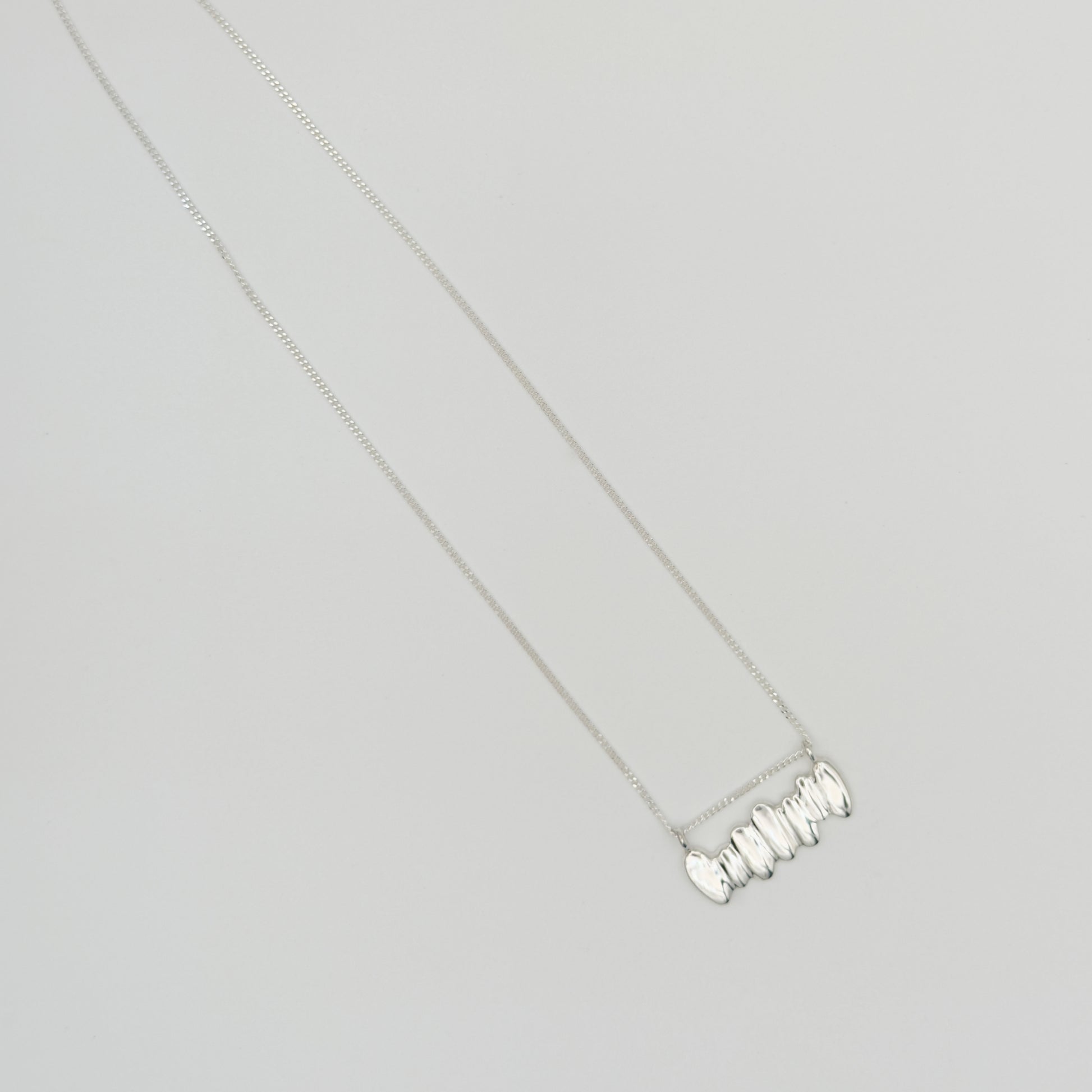Top view of the Meridian textured silver necklace, pictured on a light plain background.