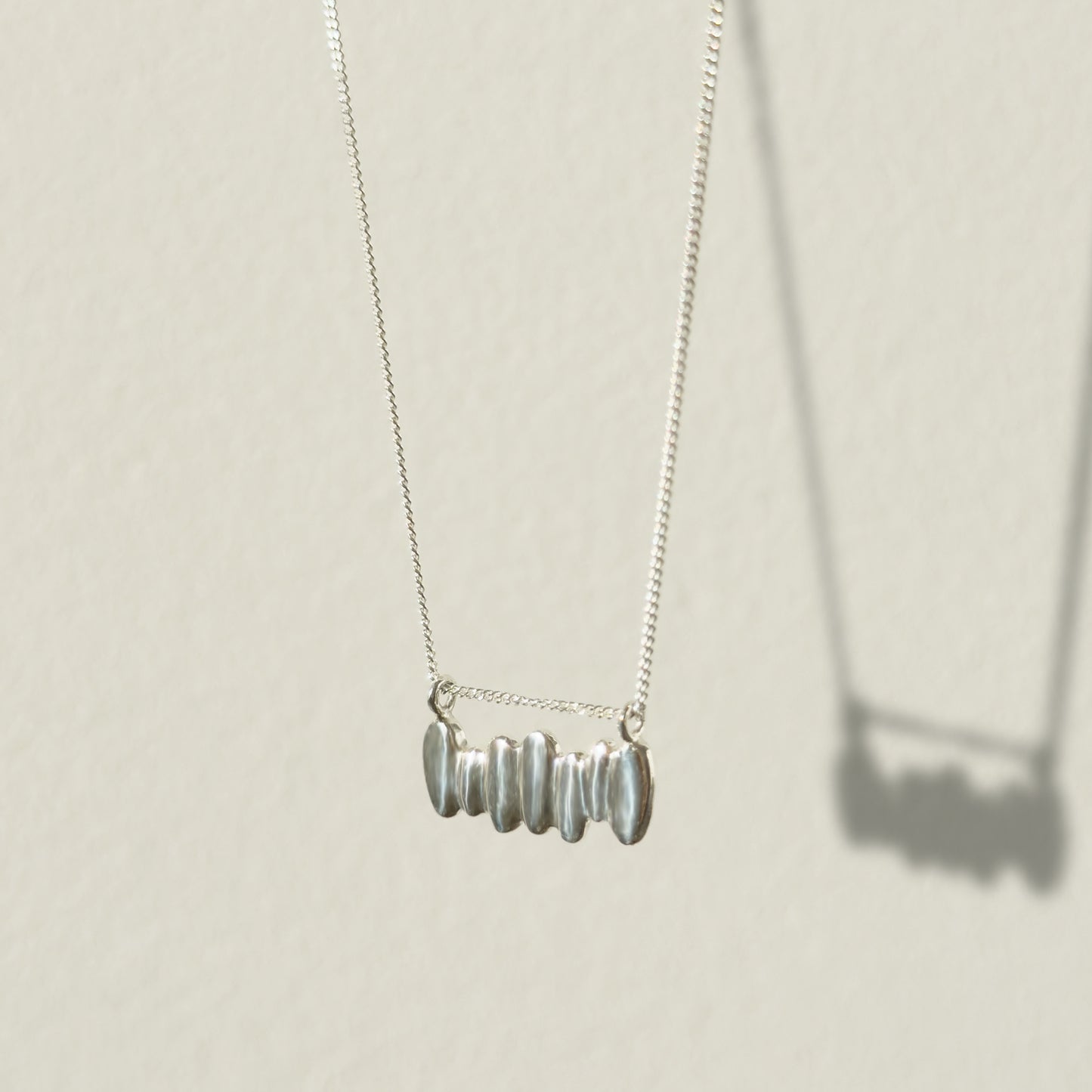 Angled front view of the Meridian textured silver necklace, pictured on a light plain background.