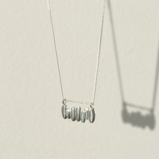Angled front view of the Meridian textured silver necklace, pictured on a light plain background.