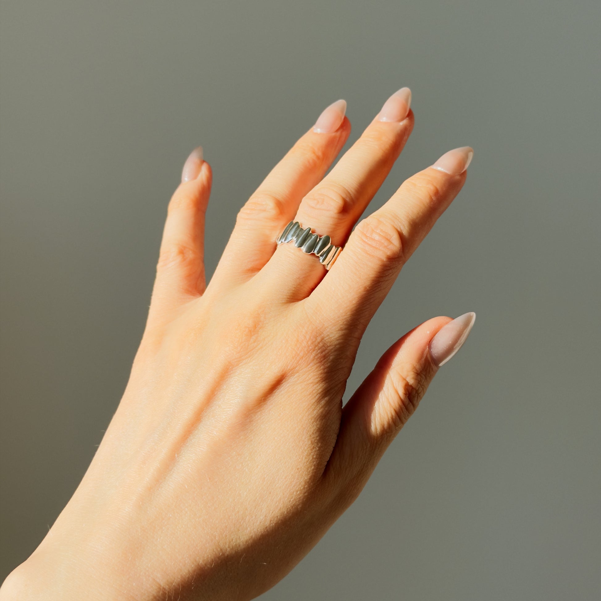 Hand wearing the Meridian textured silver ring in the sunlight, on a plain gray background.