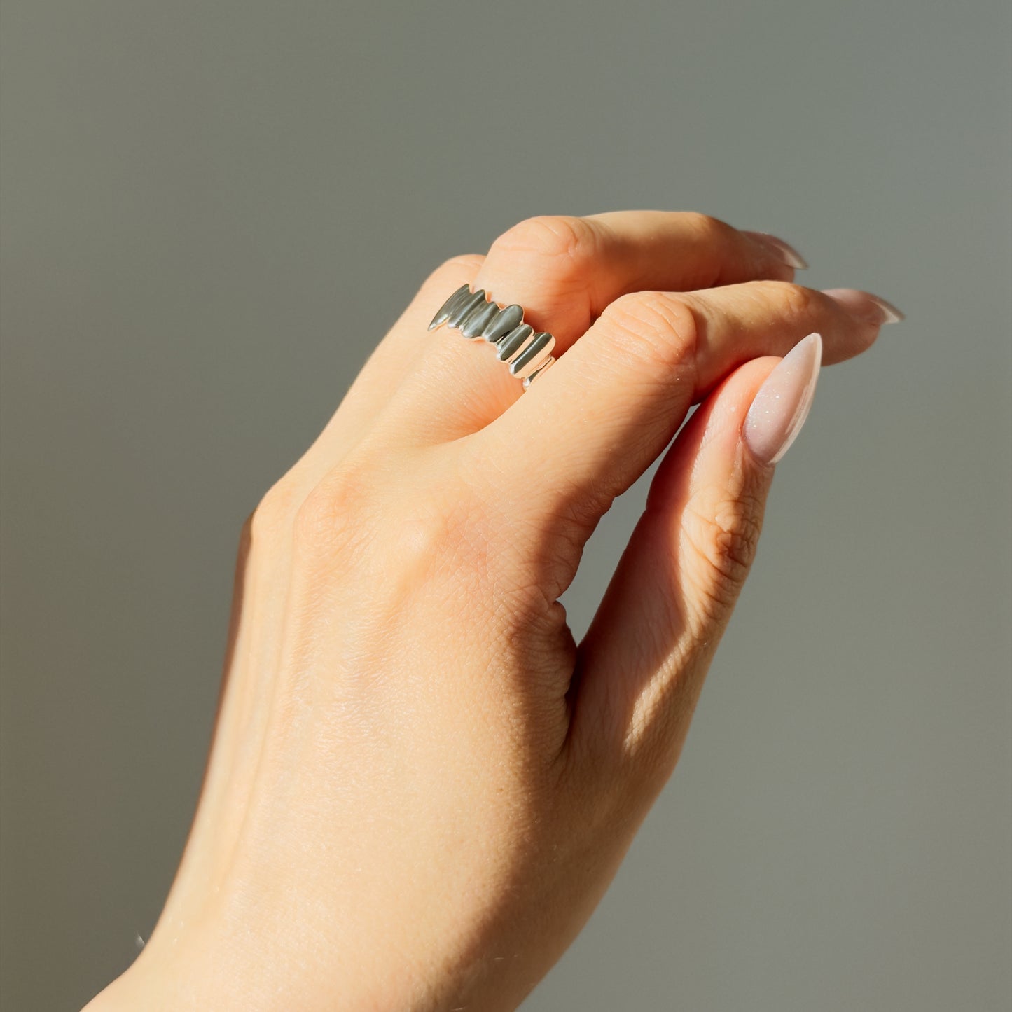 Hand wearing the Meridian textured silver ring in the sunlight, on a plain gray background.