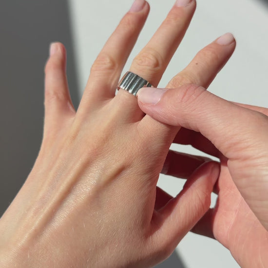 A close up of a hand feeling the texture of the Wave ring. Pictured on a light gray background.