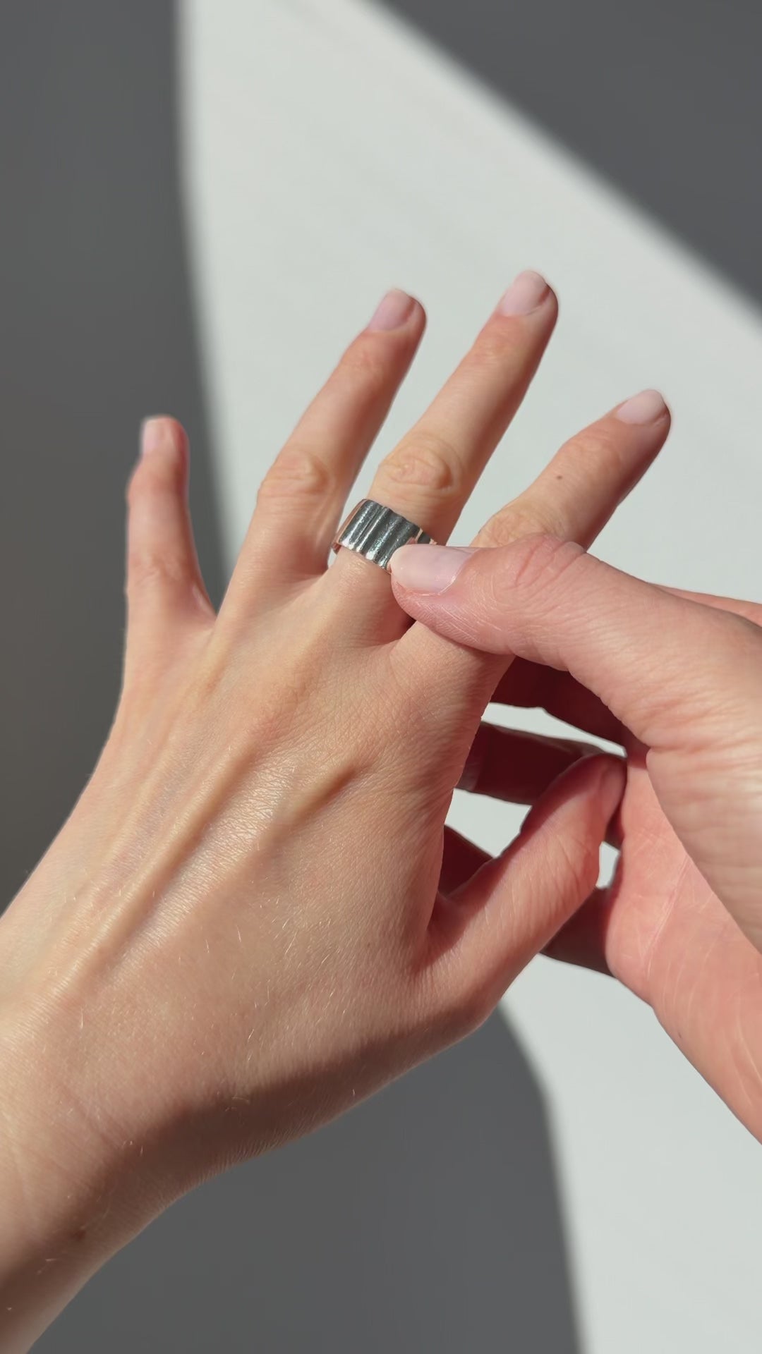 A close up of a hand feeling the texture of the Wave ring. Pictured on a light gray background.