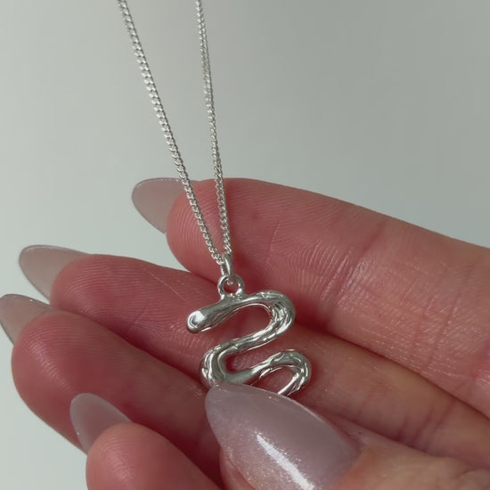 A close up of a hand feeling the texture of the Unfold necklace. Pictured on a light background.