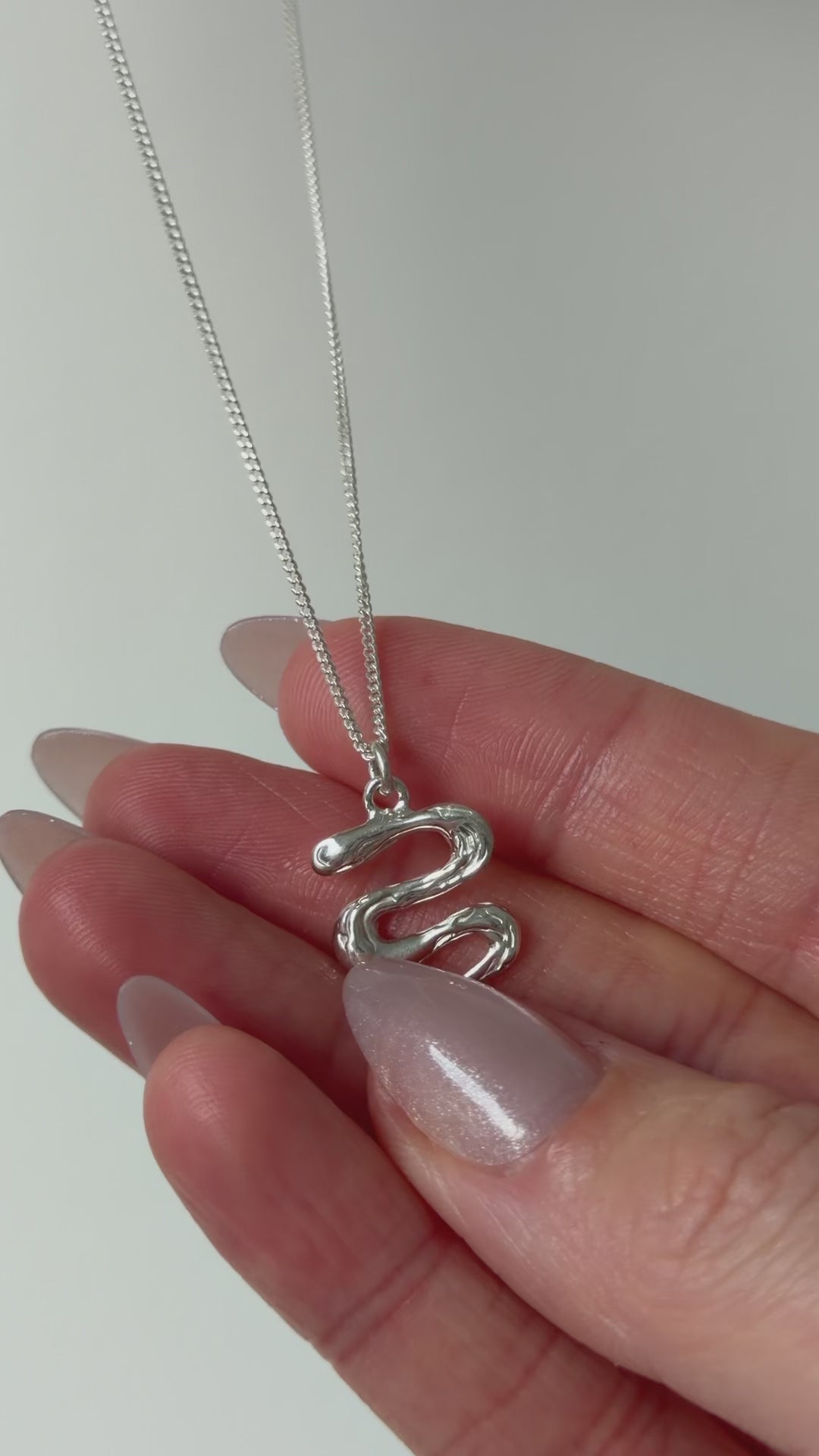 A close up of a hand feeling the texture of the Unfold necklace. Pictured on a light background.