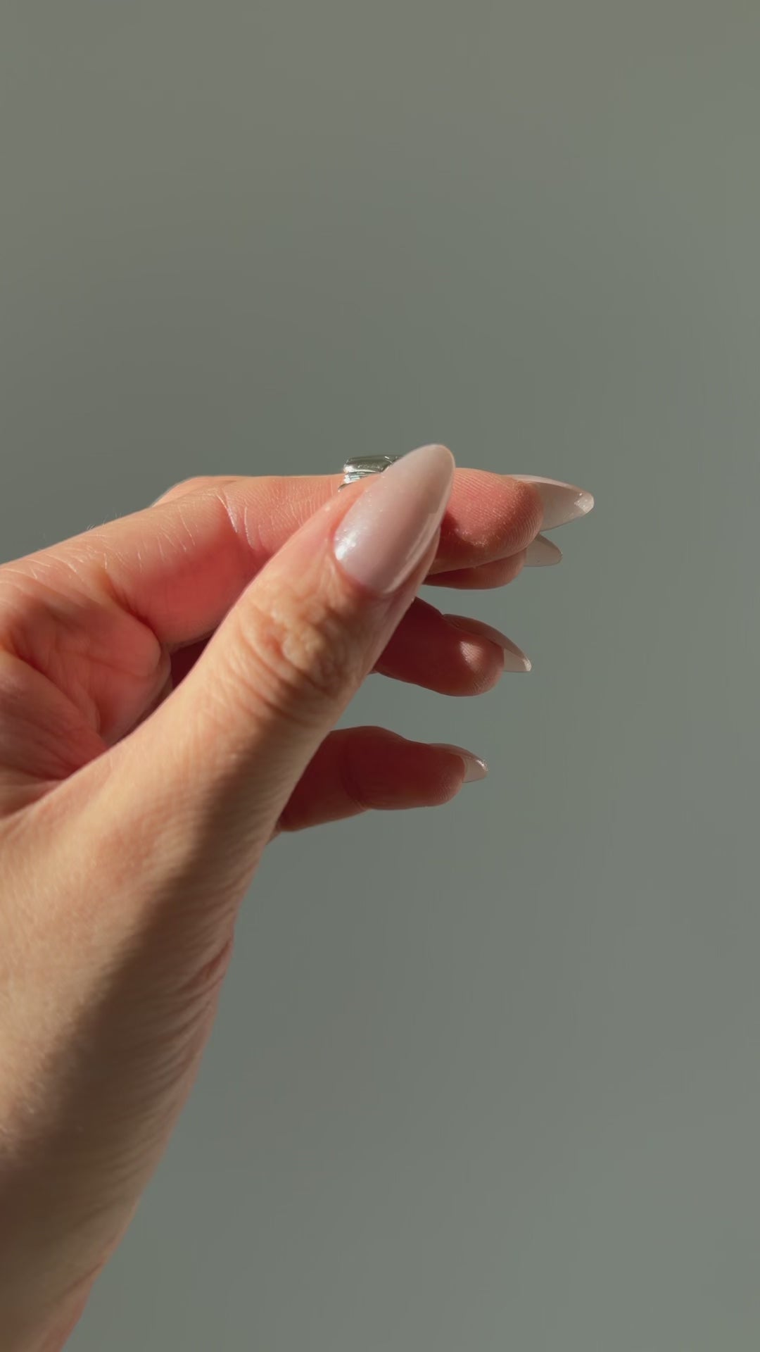 A close up of a hand feeling the texture of the Meridian ring. Pictured on a light gray background.