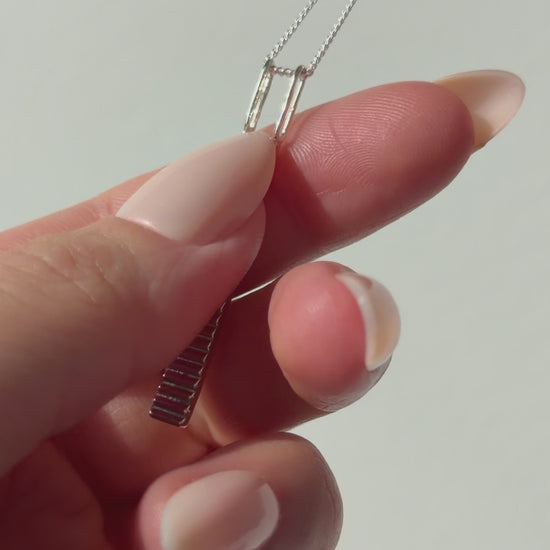 A close up of a hand feeling the texture of the Thread necklace. Pictured on a light background.