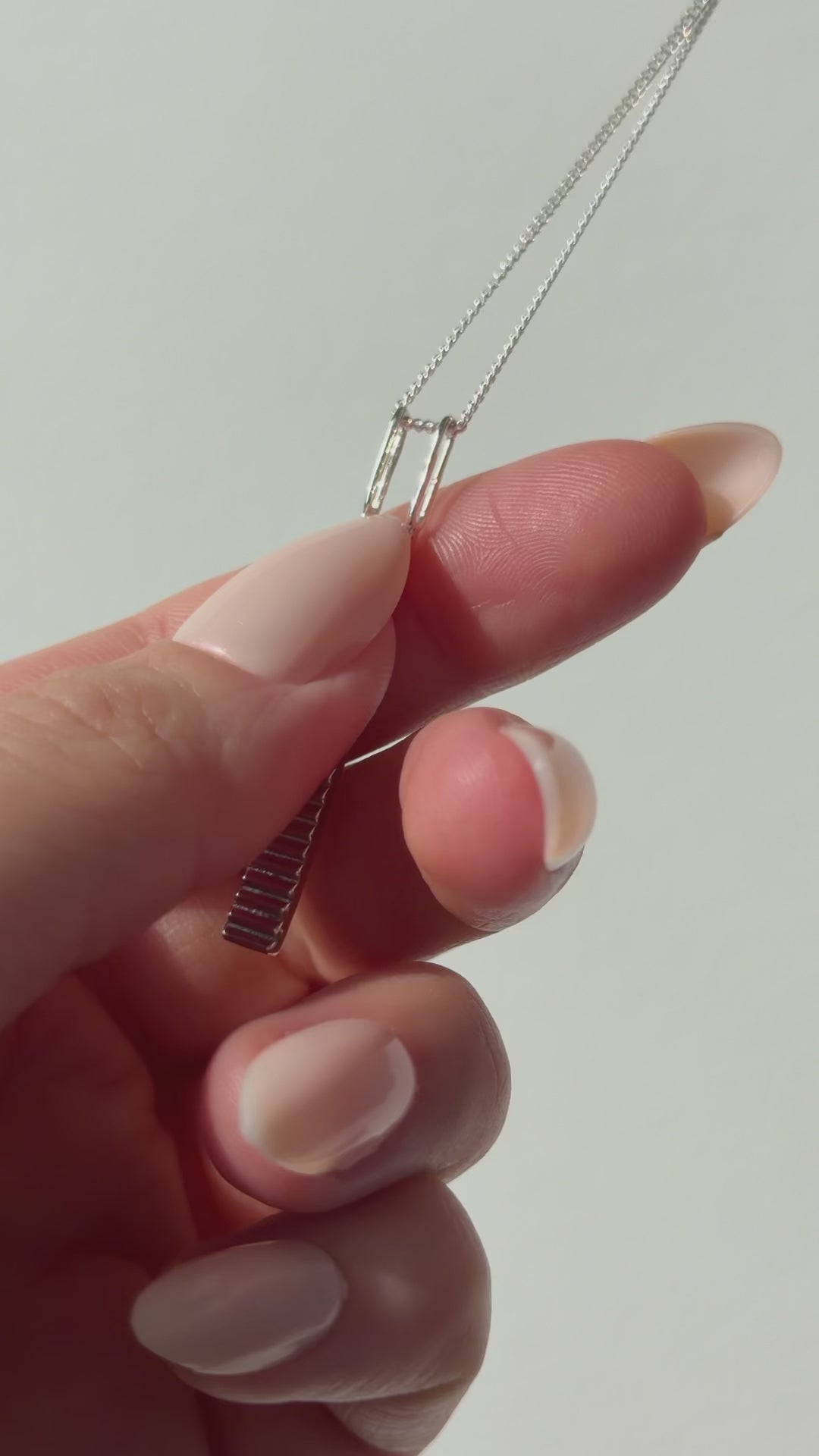 A close up of a hand feeling the texture of the Thread necklace. Pictured on a light background.