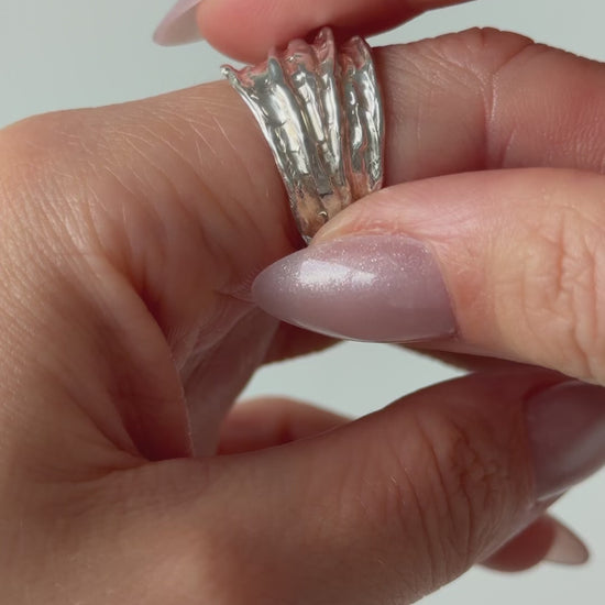 A close up of a hand feeling the texture of the Canyon ring. Pictured on a light background.