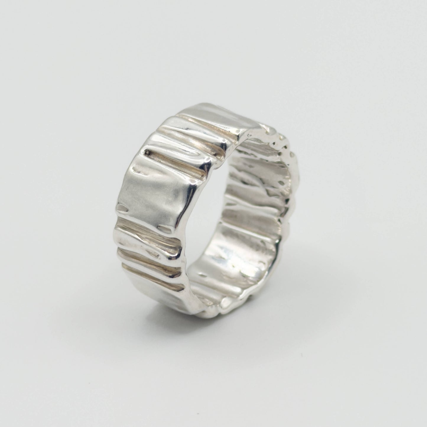 Hand wearing the Ripple silver ring on a plain background.