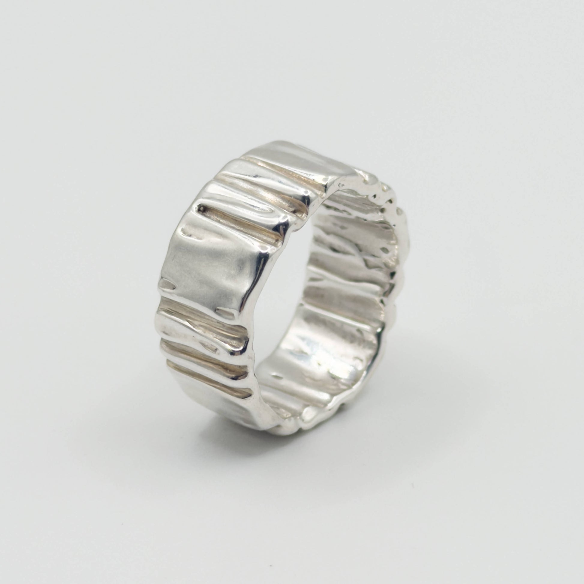 Hand wearing the Ripple silver ring on a plain background.