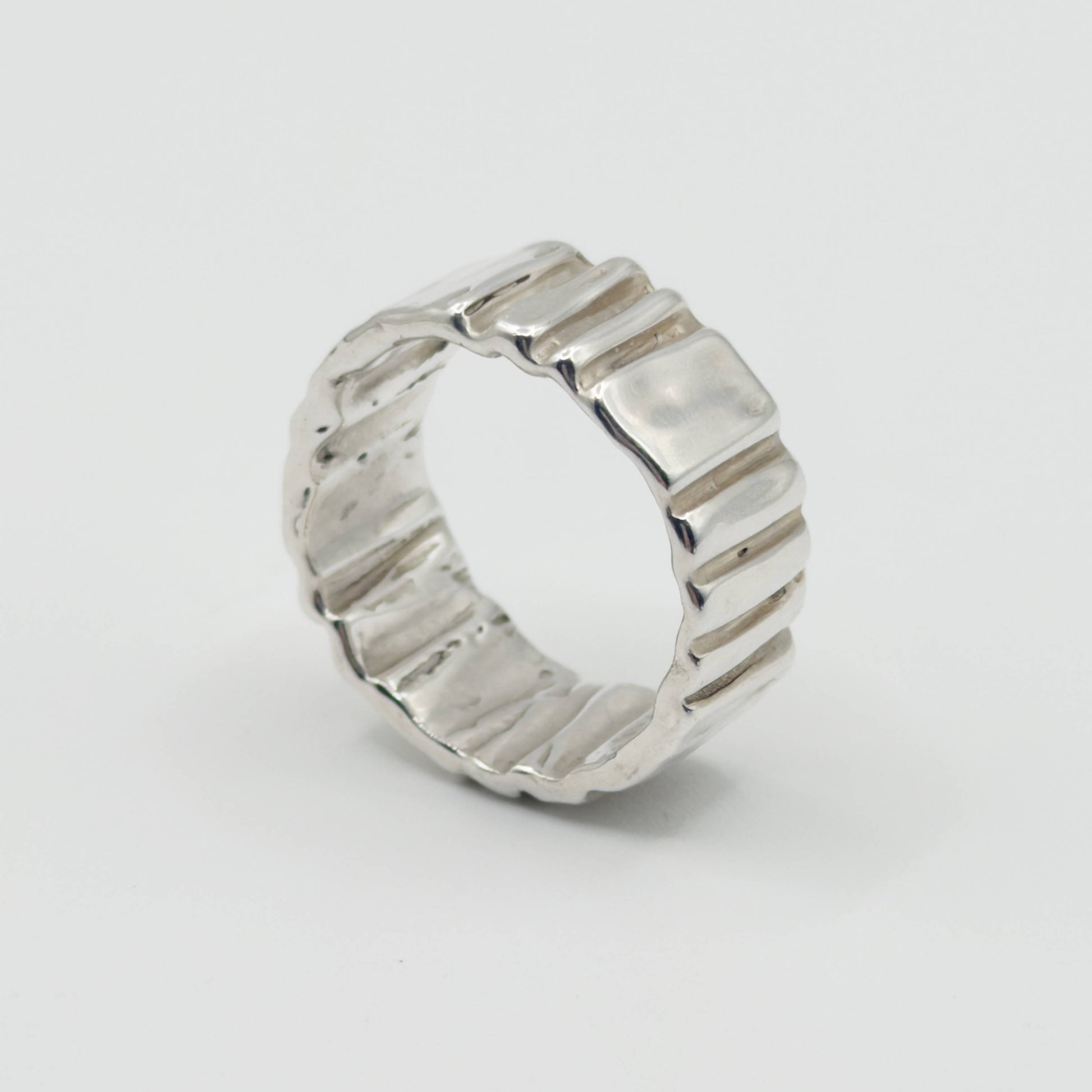 Angled side view of the Ripple silver ring, pictured on a light plain background.