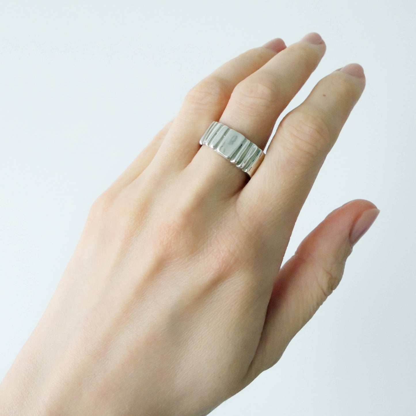 Hand wearing the Ripple silver ring on a plain background.
