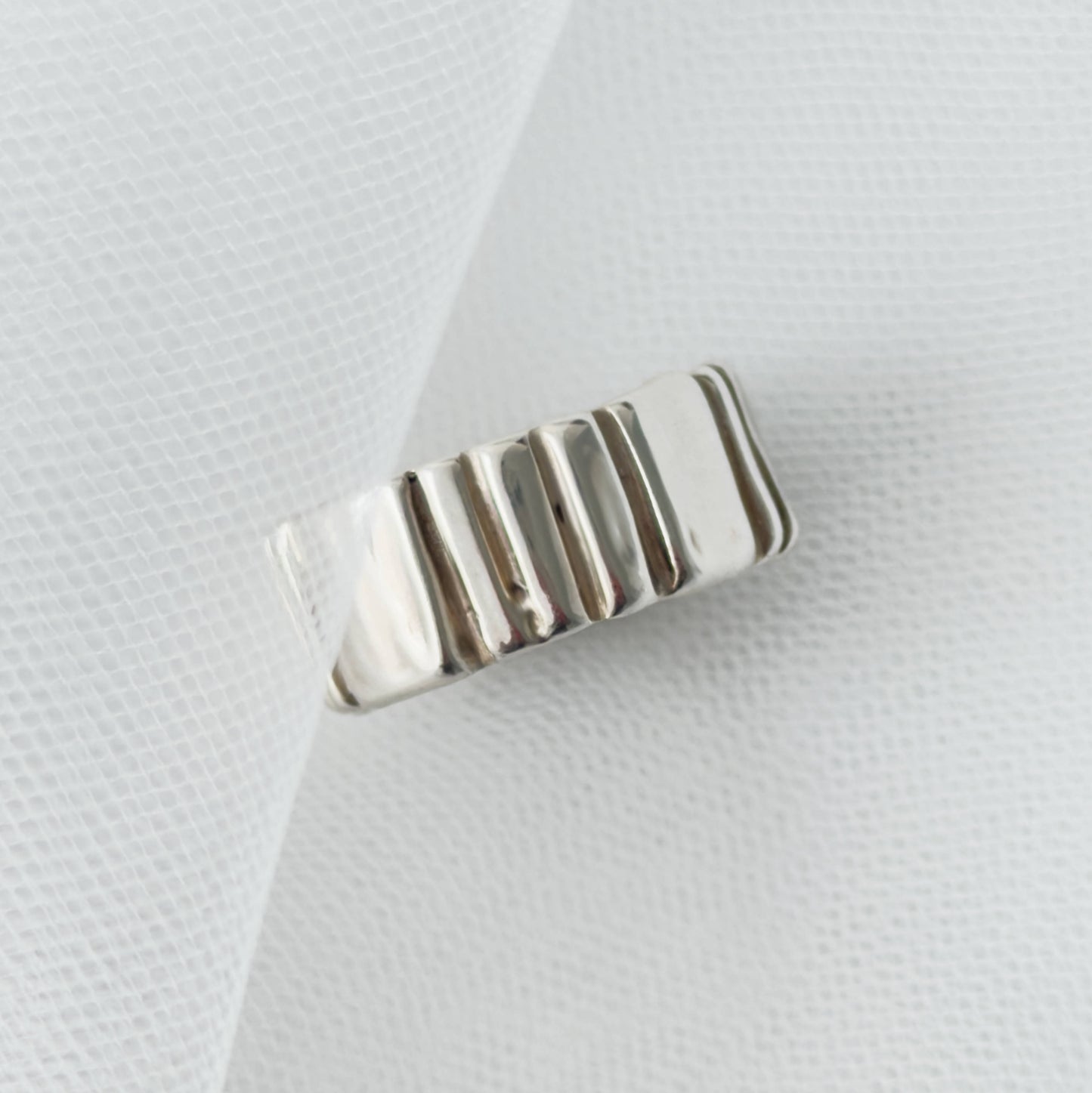 Front view of the Ripple silver ring, pictured on a light textured background.