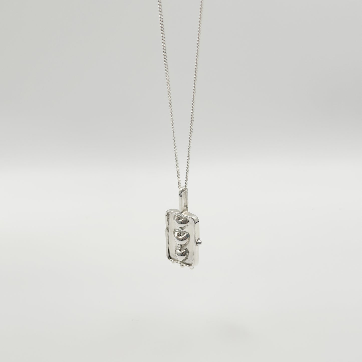 Angled front view of the Self-Compassion textured silver pendant on a curb chain, pictured on a light plain background.