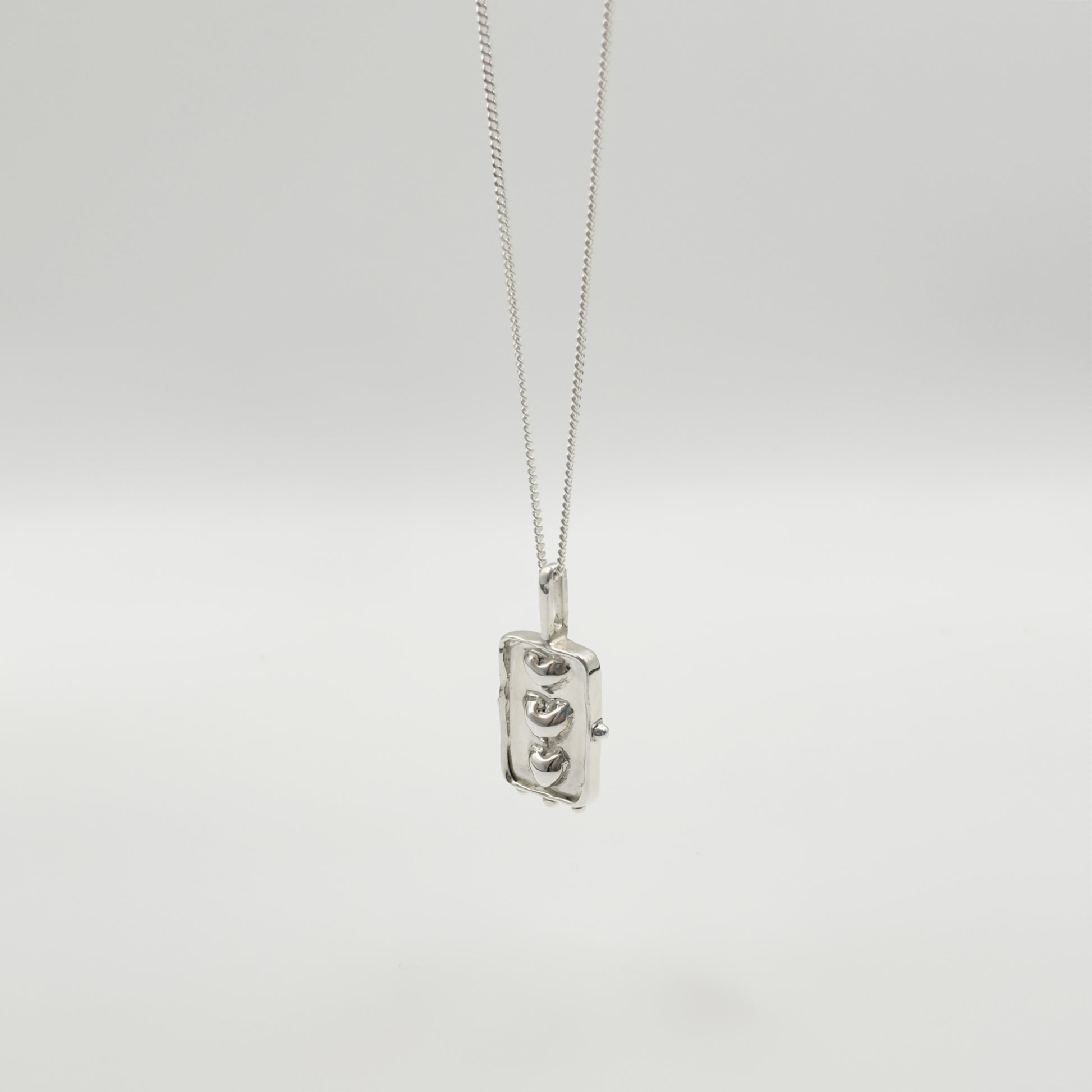 Angled front view of the Self-Compassion textured silver pendant on a curb chain, pictured on a light plain background.