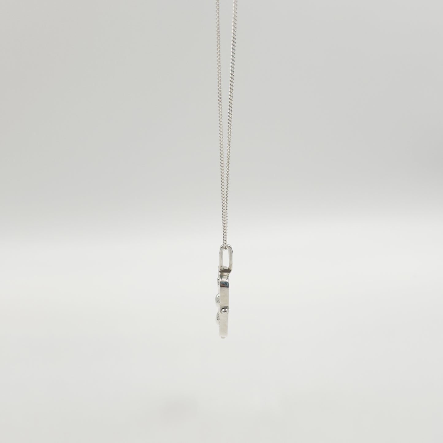 Side view of the Self-Compassion textured silver pendant on a curb chain, pictured on a light plain background.