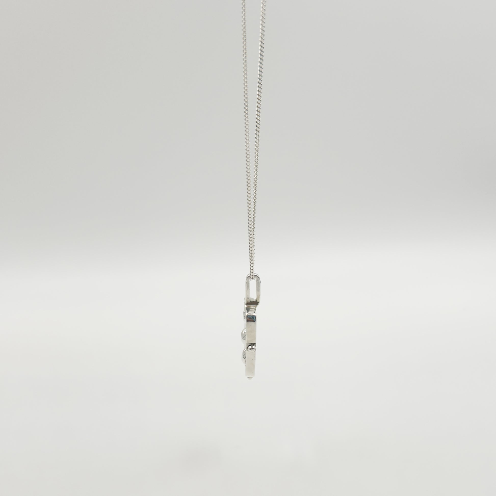 Side view of the Self-Compassion textured silver pendant on a curb chain, pictured on a light plain background.
