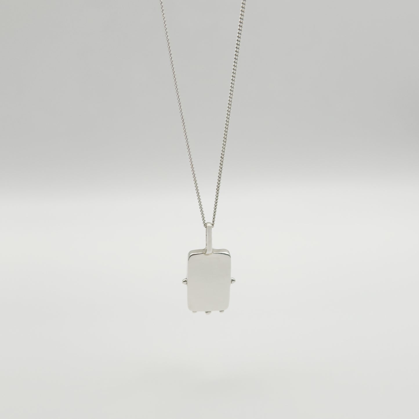 Back view of the Self-Compassion textured silver pendant on a curb chain, pictured on a light plain background.