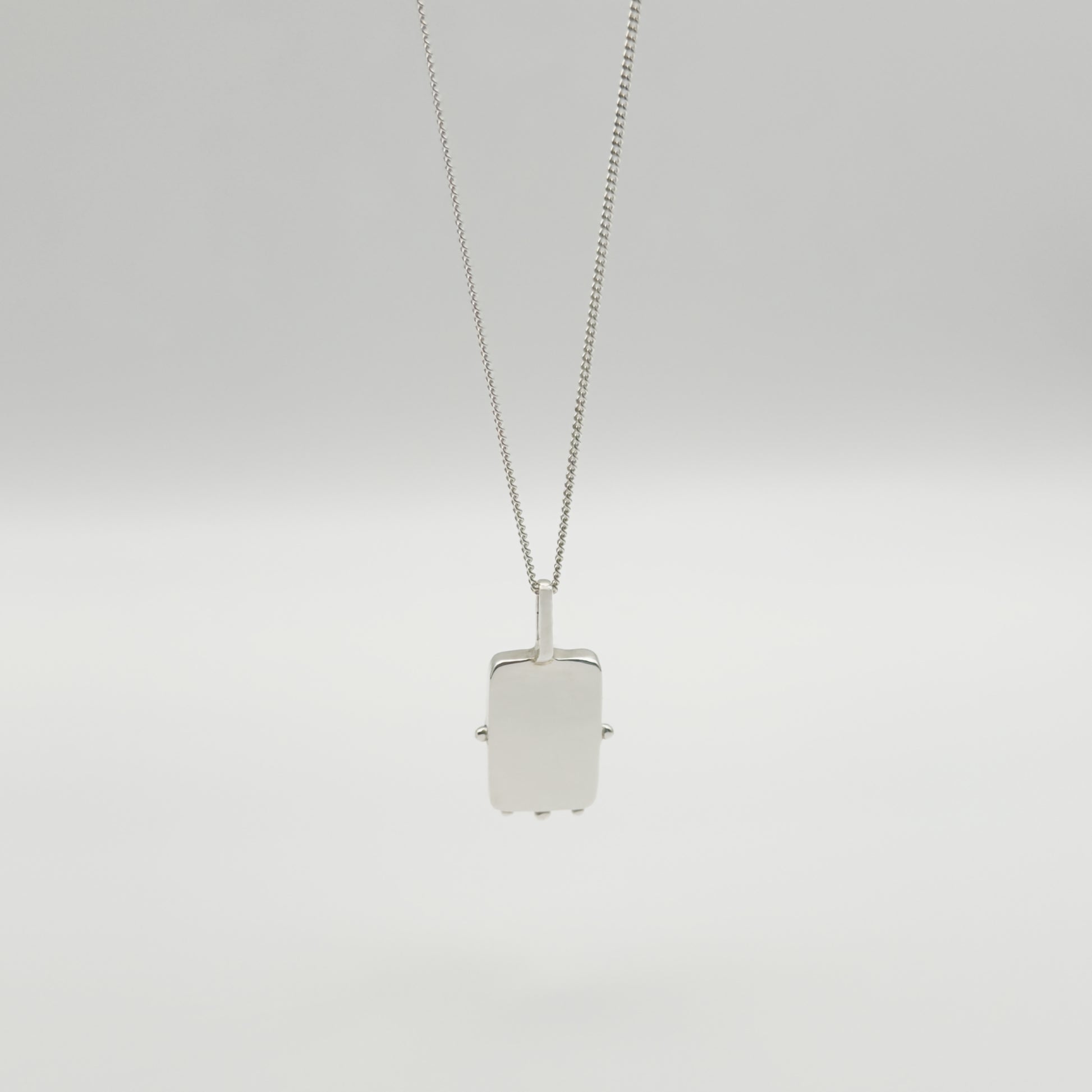 Back view of the Self-Compassion textured silver pendant on a curb chain, pictured on a light plain background.