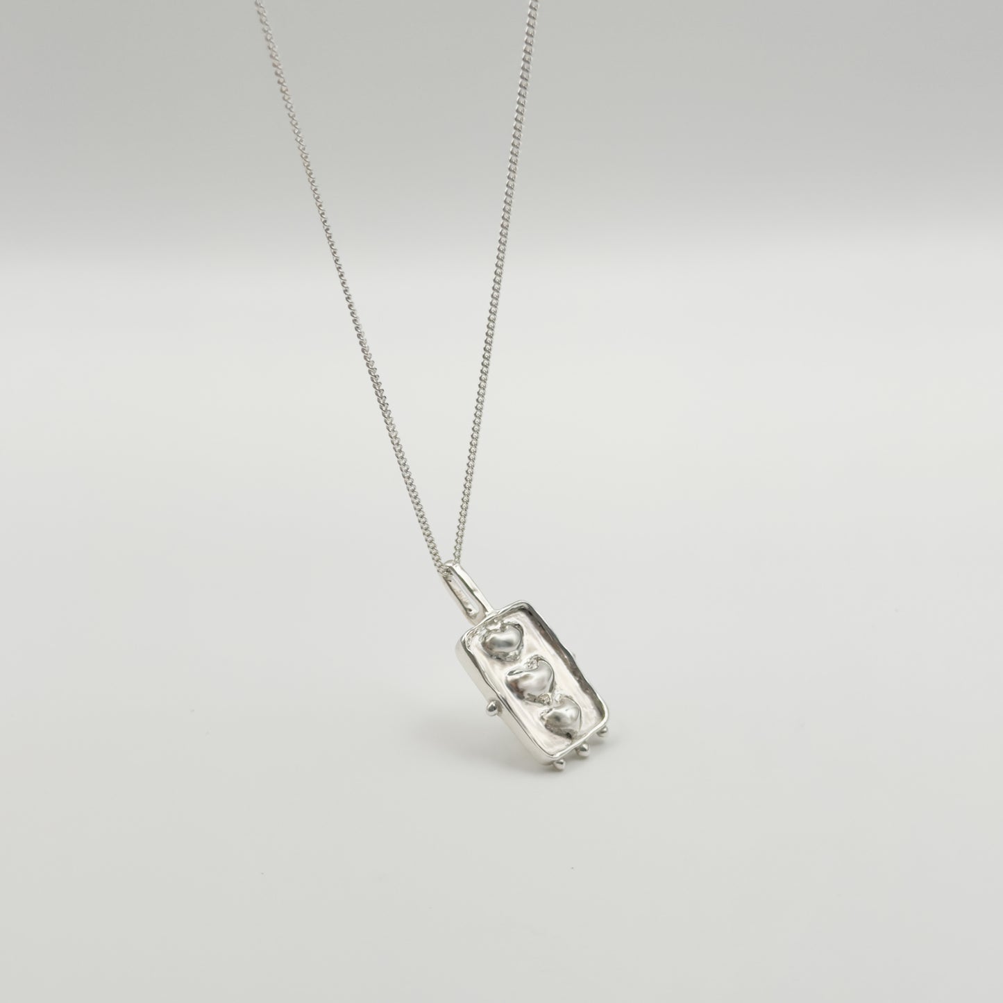 Angled front view of the Self-Compassion textured silver pendant on a curb chain, pictured on a light plain background.